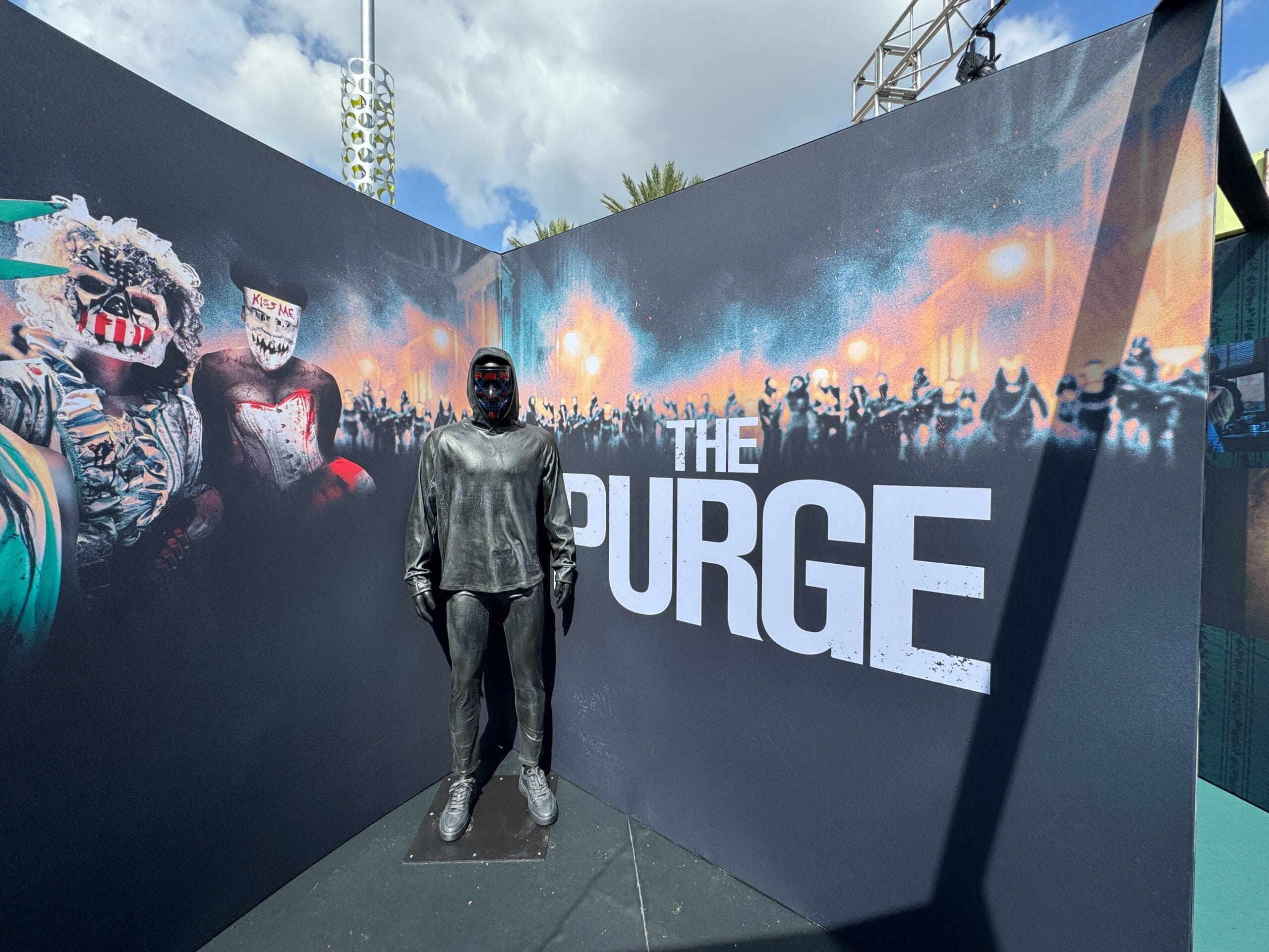A person in a black costume stands by a “The Purge” Blumhouse display at Universal CityWalk.