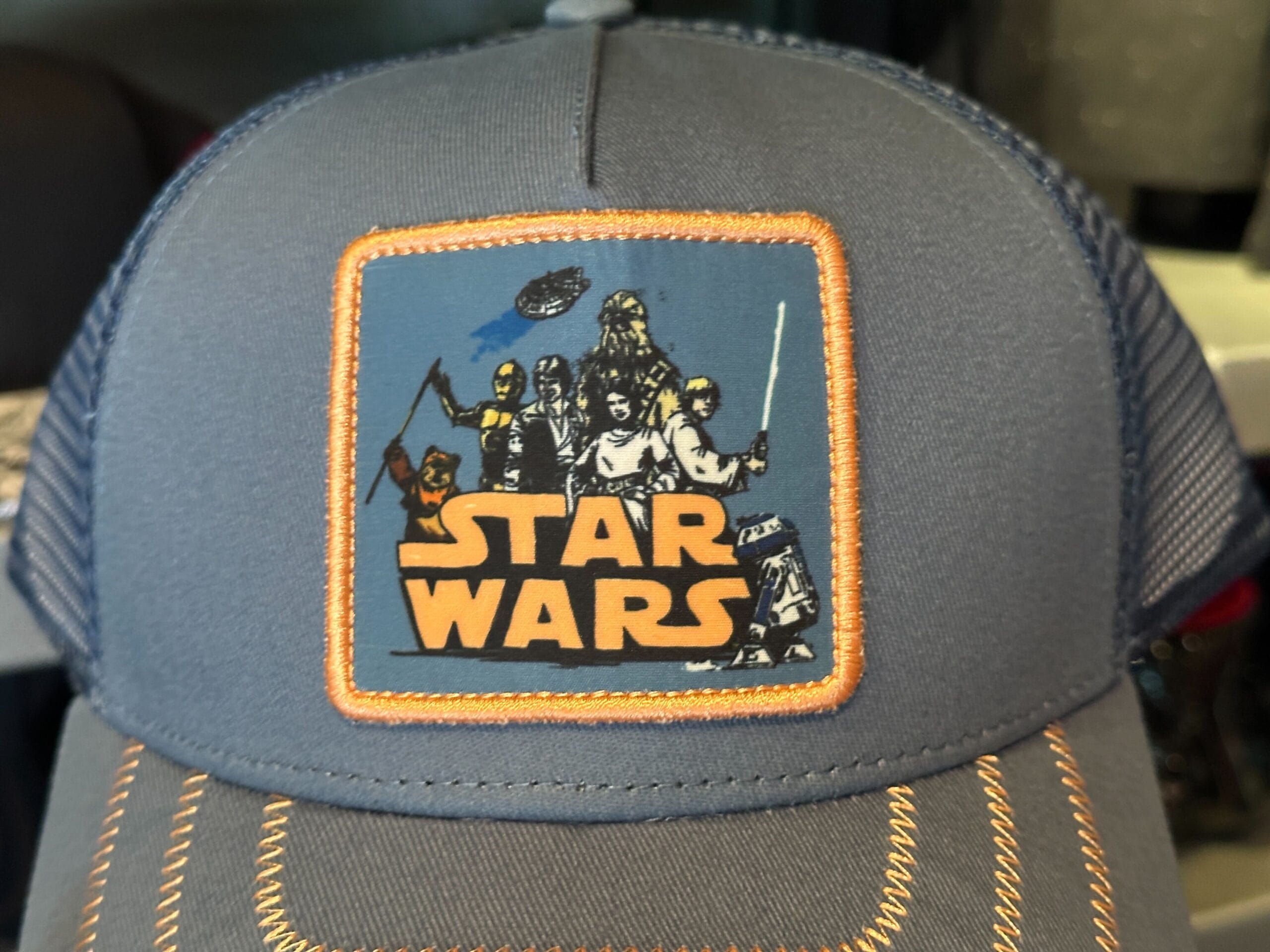 A blue cap with a Star Wars patch featuring heroic Rebel Alliance characters and the logo in orange letters.