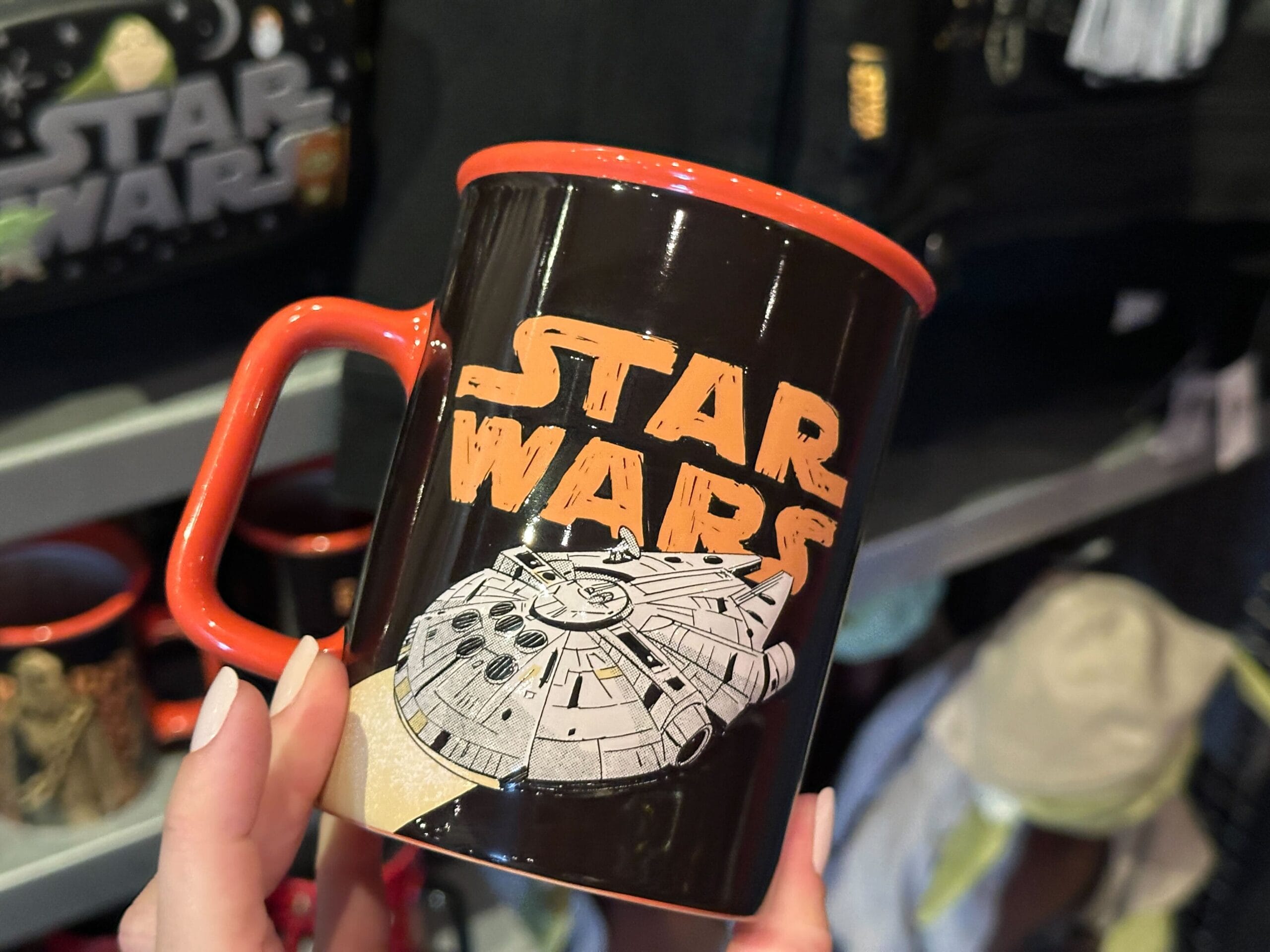 A hand holds a black Star Wars mug with the Millennium Falcon, orange Star Wars logo, and orange rim and handle.