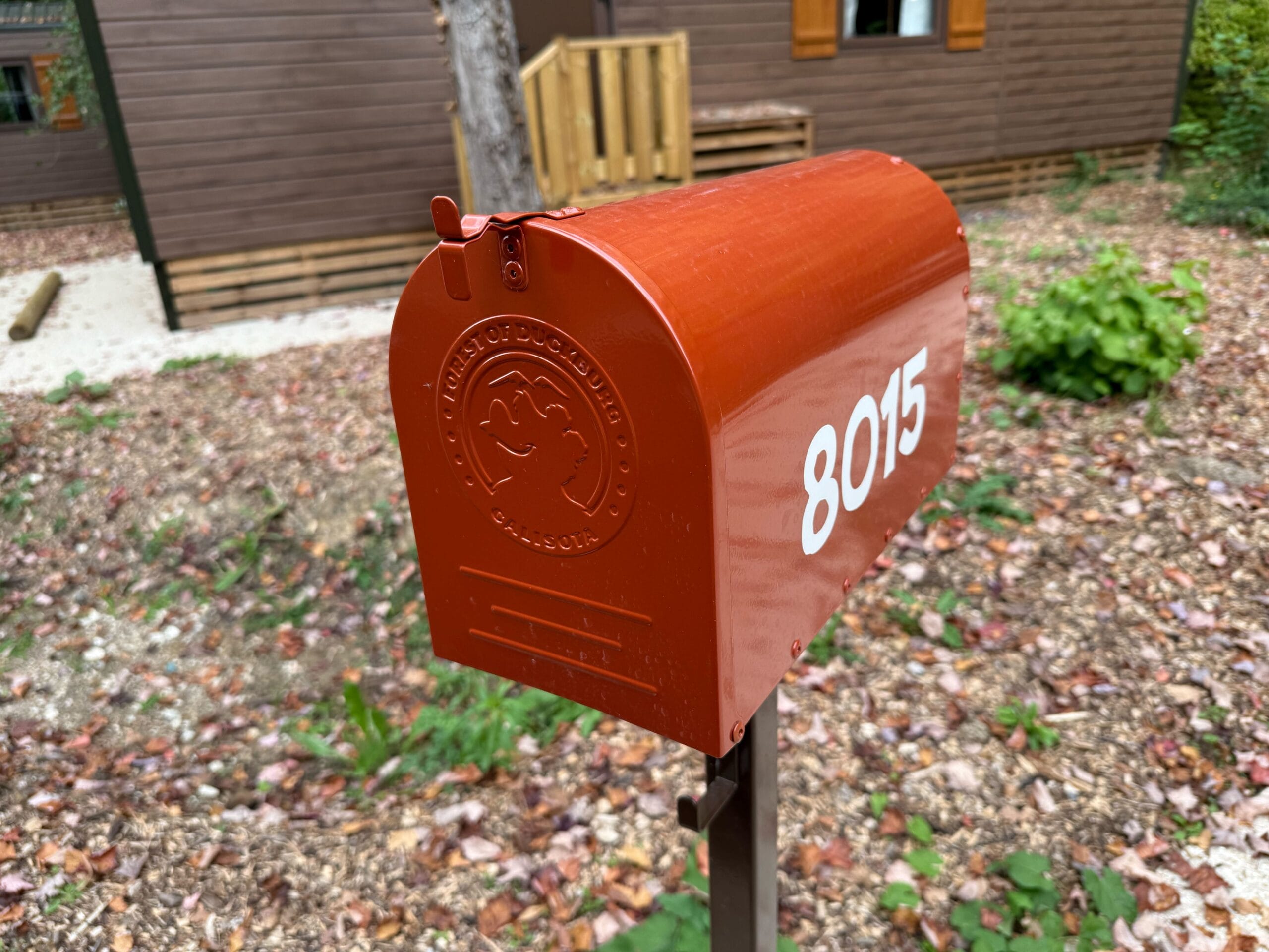 A red metal mailbox with "8015" on the side and a front embossed image that says "Forest of Duckburg Calisota" around a cartoon bear silhouette.