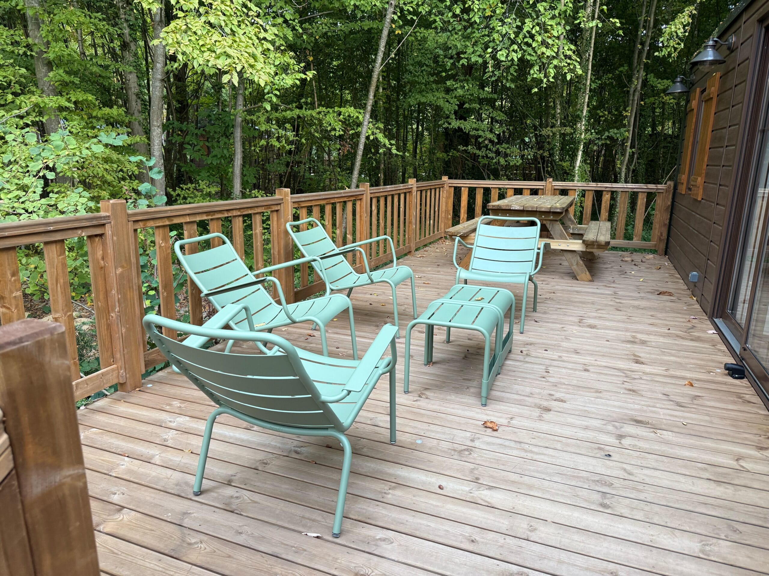 Wooden patio outside a cabin at Davy Crockett Ranch in Disneyland Paris, featuring green metal chairs and tables.