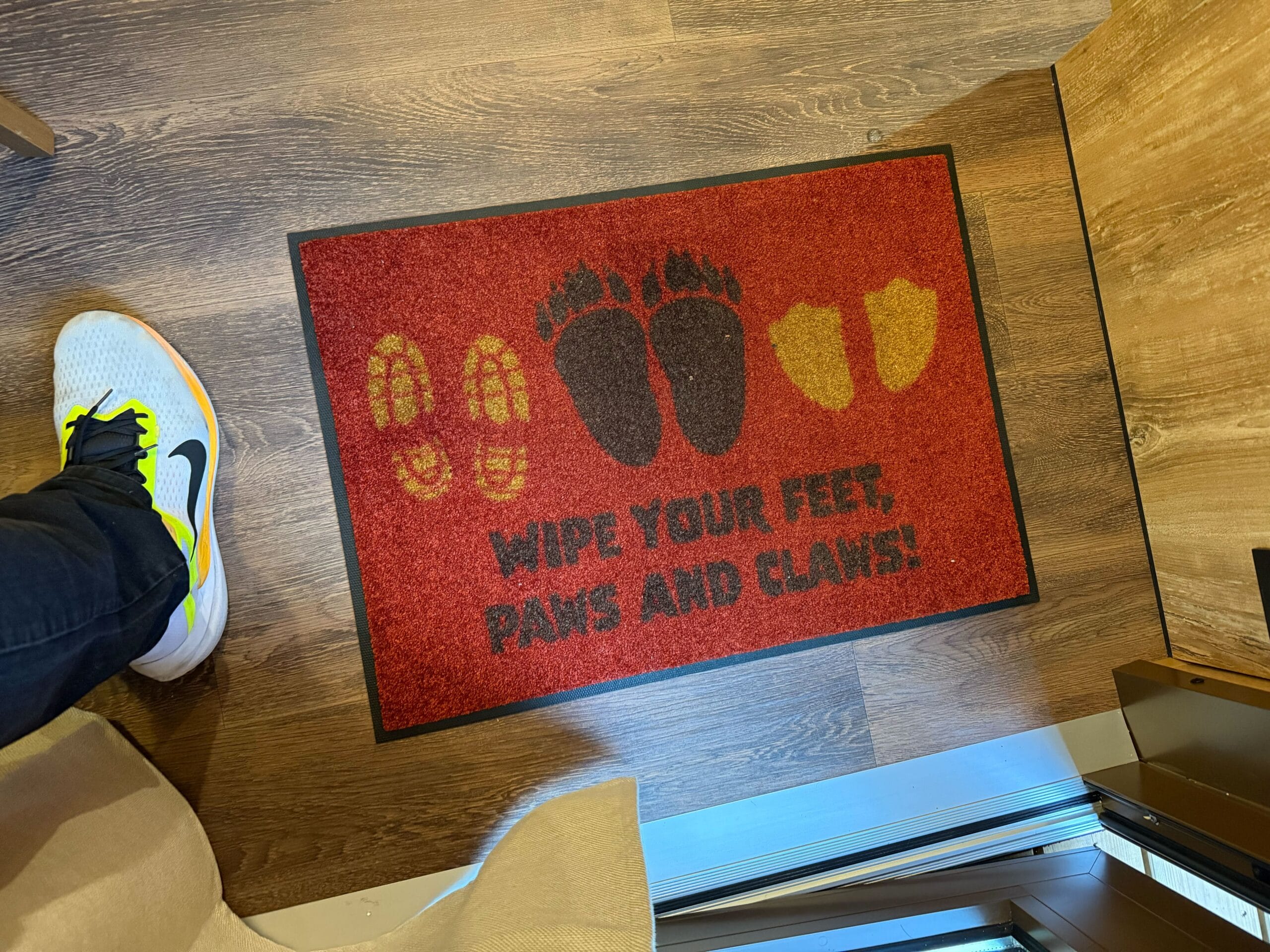 Red doormat with boot, bear paw, and duck prints and the words "Wipe your feet, paws and claws!" in a cabin at Davy Crockett Ranch at Disneyland Paris.