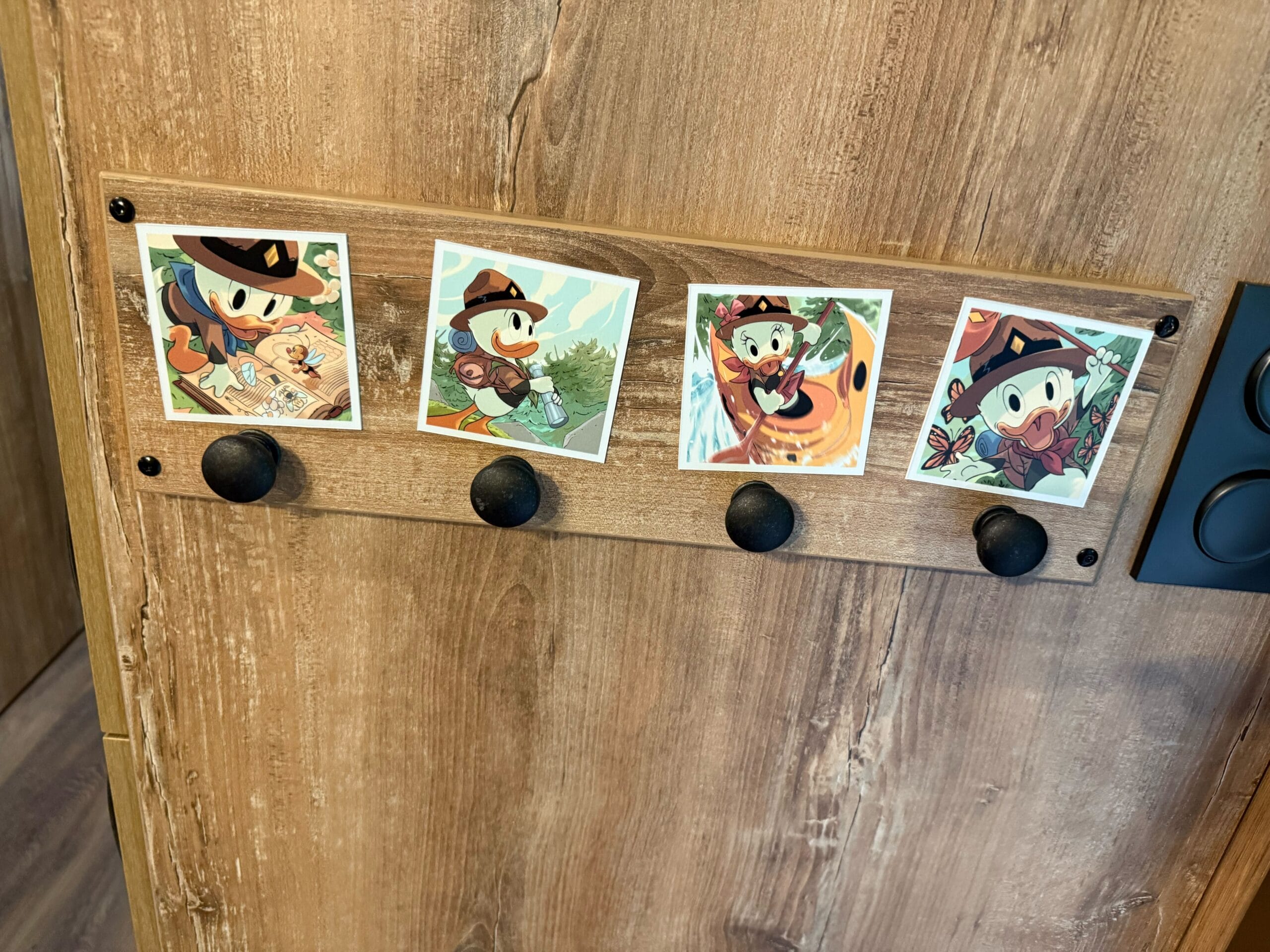 Four "Polaroids" of Huey, Dewey, Louie, and Webby Vanderquack hang above black coat hooks in a Davy Crockett Ranch cabin.