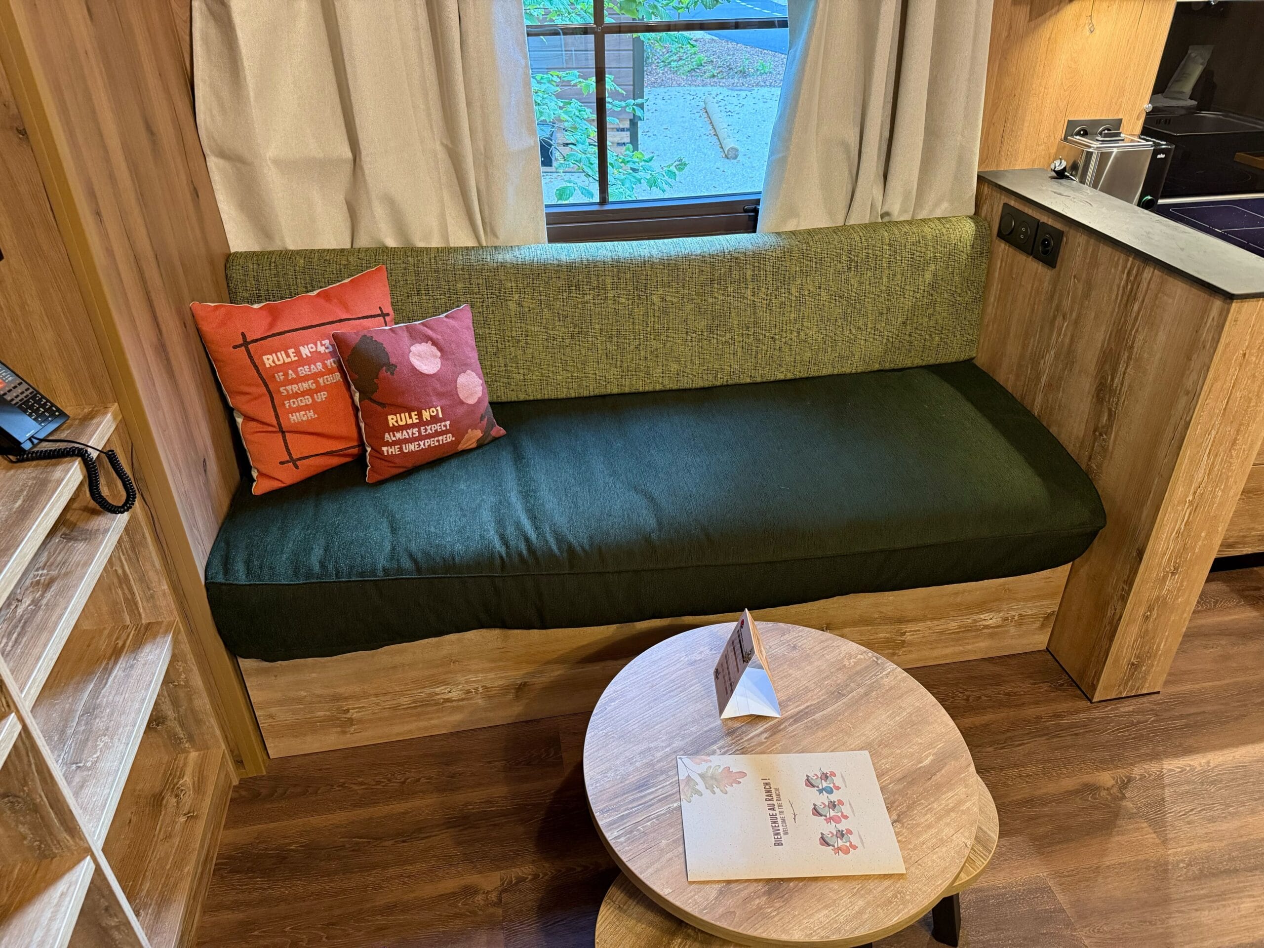 Cozy cabin room at Davy Crockett Ranch with a green bench, pillows, a round table, and curtains,