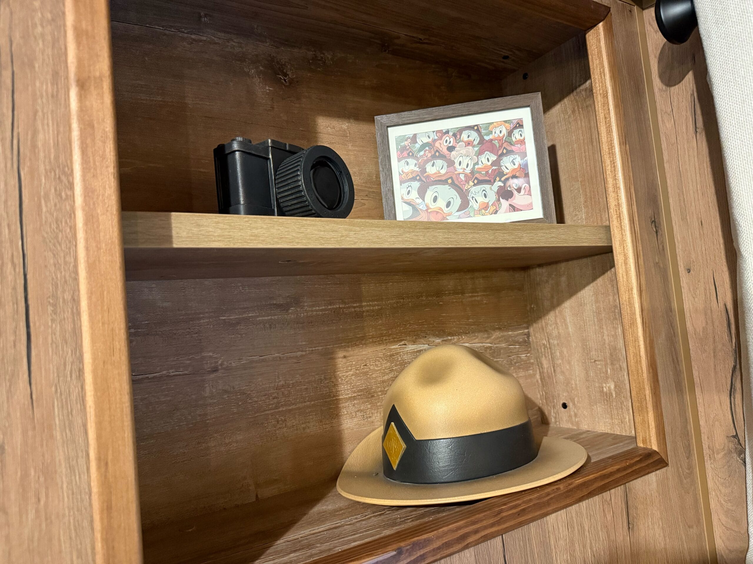 A wooden shelf in a Davy Crockett Ranch cabin displays a vintage camera, Junior Woodchucks group "photo," and ranger hat.