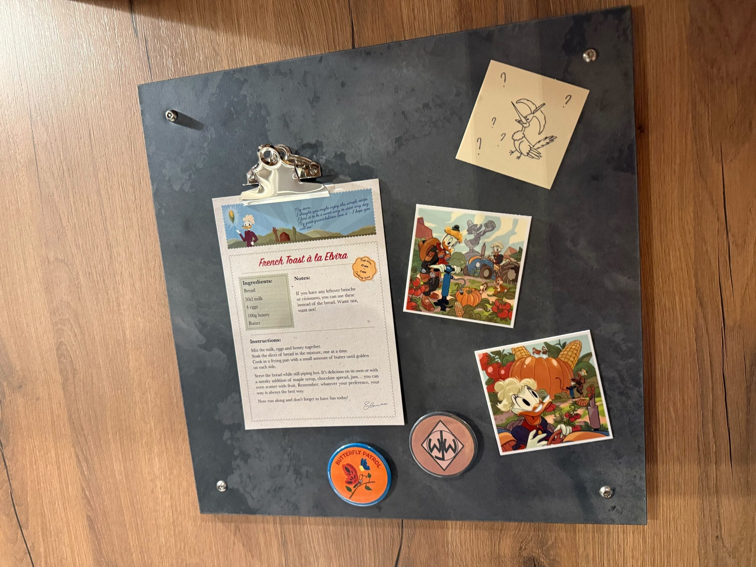 A metal board with a french toast recipe, "photos" of Grandpa and Grandma Duck, and Junior Woodchucks buttons.