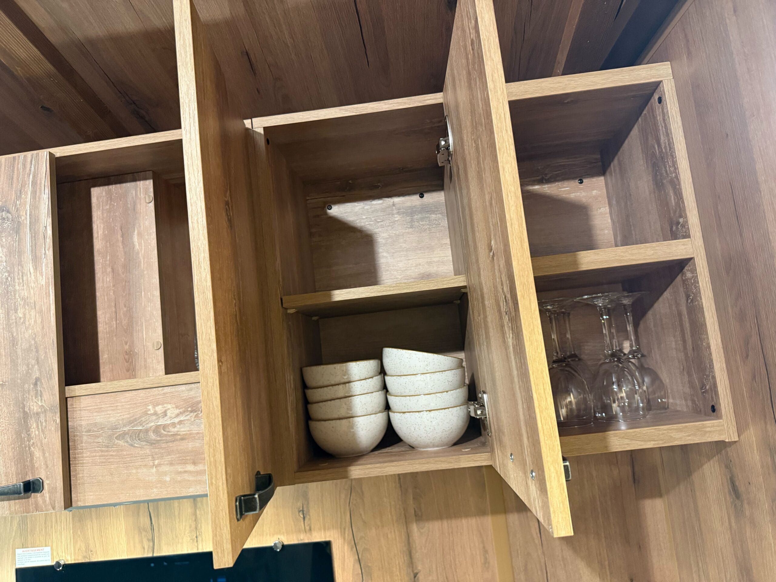 Open wooden kitchen cabinets at Davy Crockett Ranch Cabin Room in Disneyland Paris, stacked bowls, upside-down wine glasses inside.