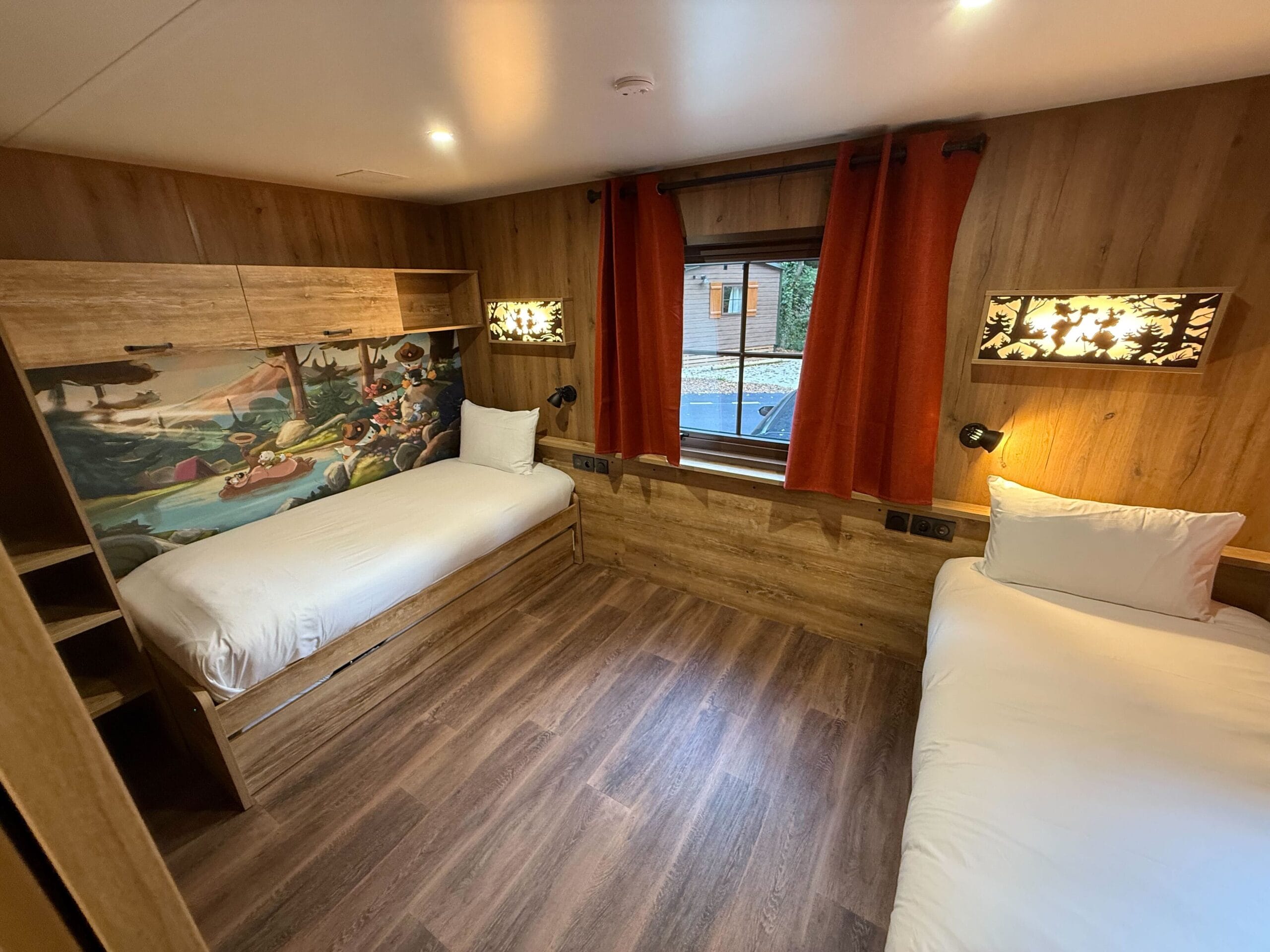 Cozy Davy Crockett Ranch cabin room near Disneyland Paris, with two single beds, wood paneling, red curtains, and a window.