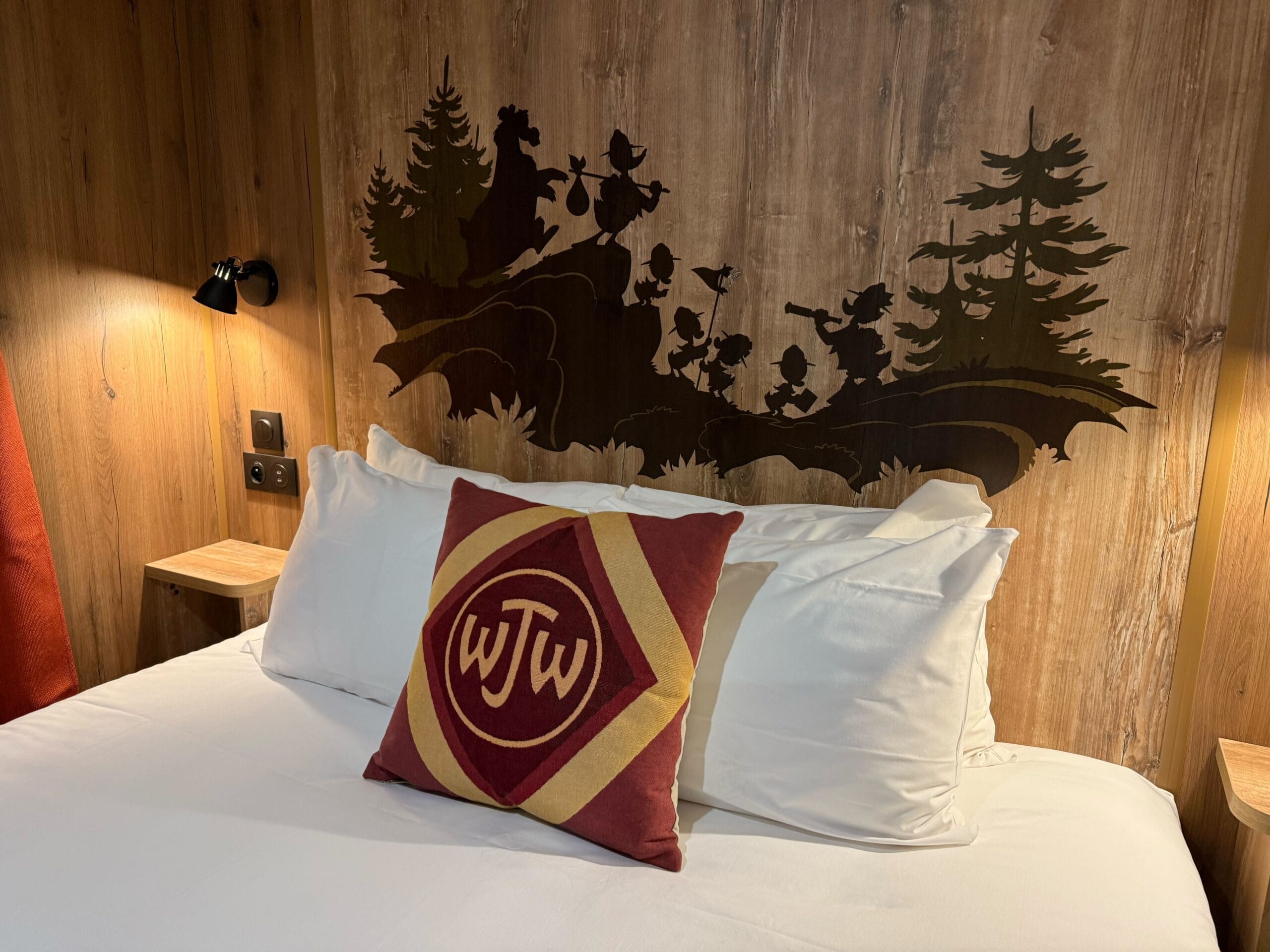 A cozy Davy Crockett Ranch cabin bed with a Junior Woodchucks monogram pillow and a mural of the Junior Woodchucks on a scouting trip.