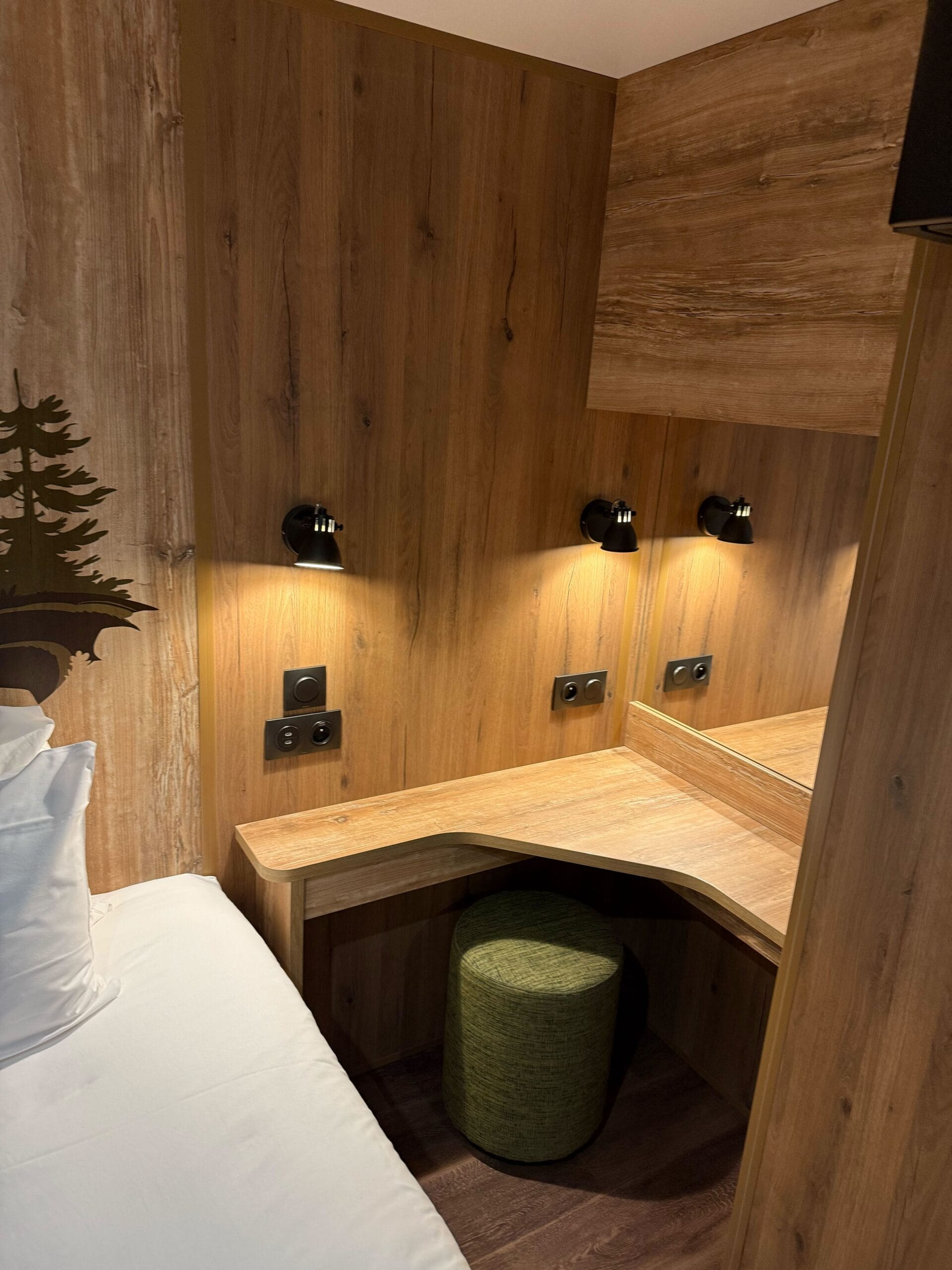 Wood-paneled Davy Crockett Ranch cabin room with a desk, mirror, and green stool.