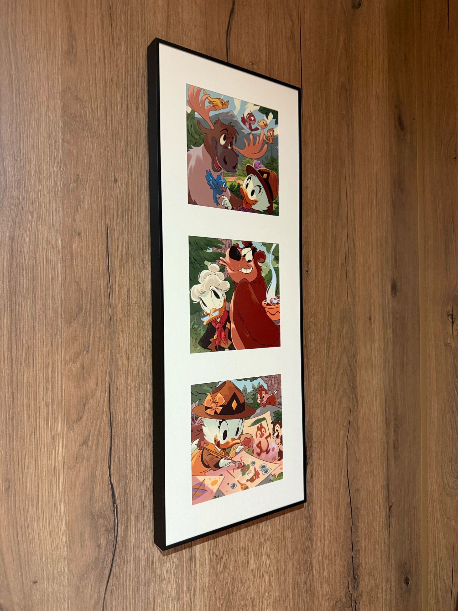 Framed triptych art of Webby Vanderquack and Grandma Duck in woodland scenes on a wood-paneled wall in a cabin at Davy Crockett Ranch in Disneyland Paris.