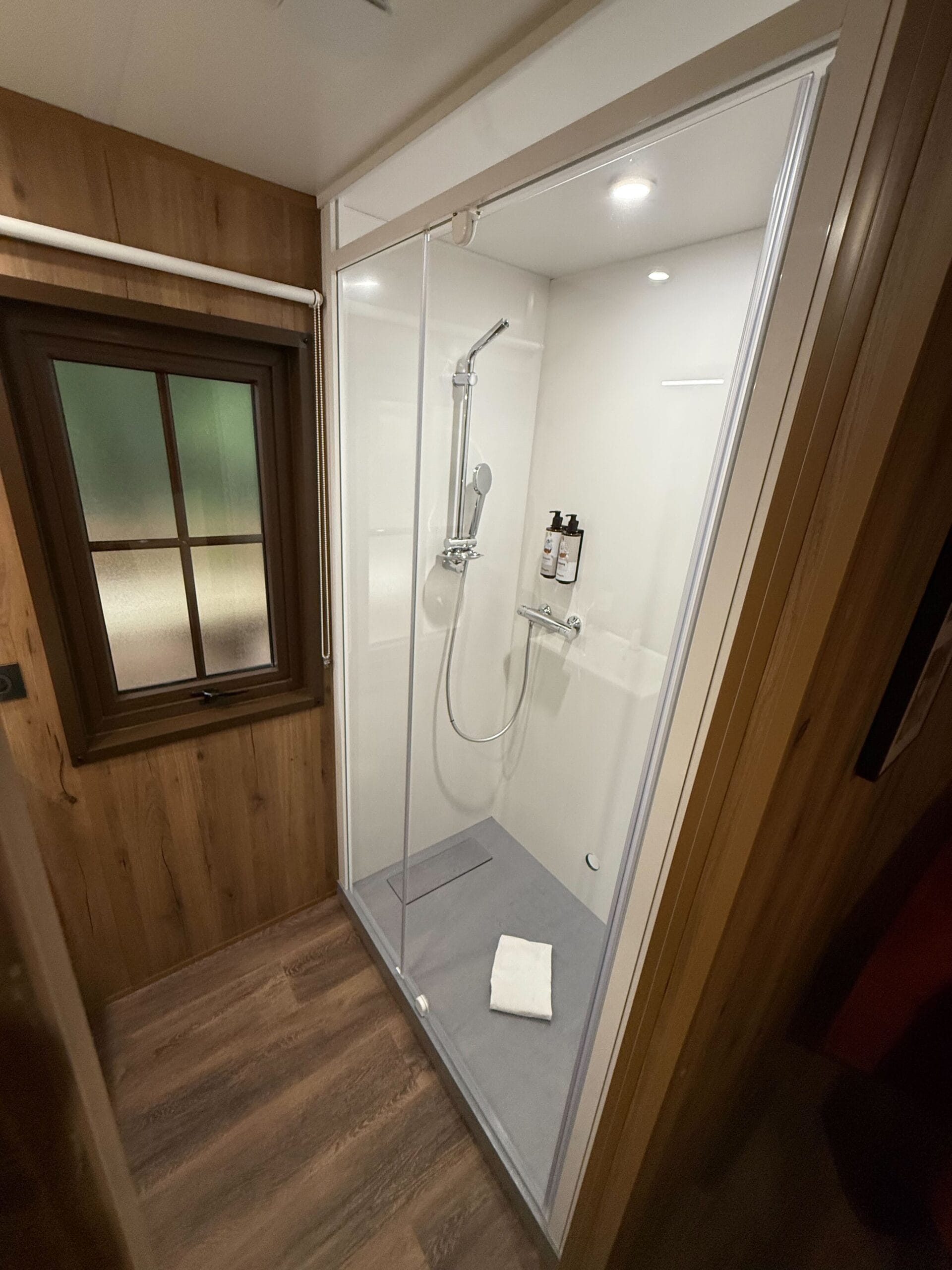 Modern shower in a Standard Cabin Room at Davy Crockett Ranch, Disneyland Paris, with glass doors and rustic wooden walls.