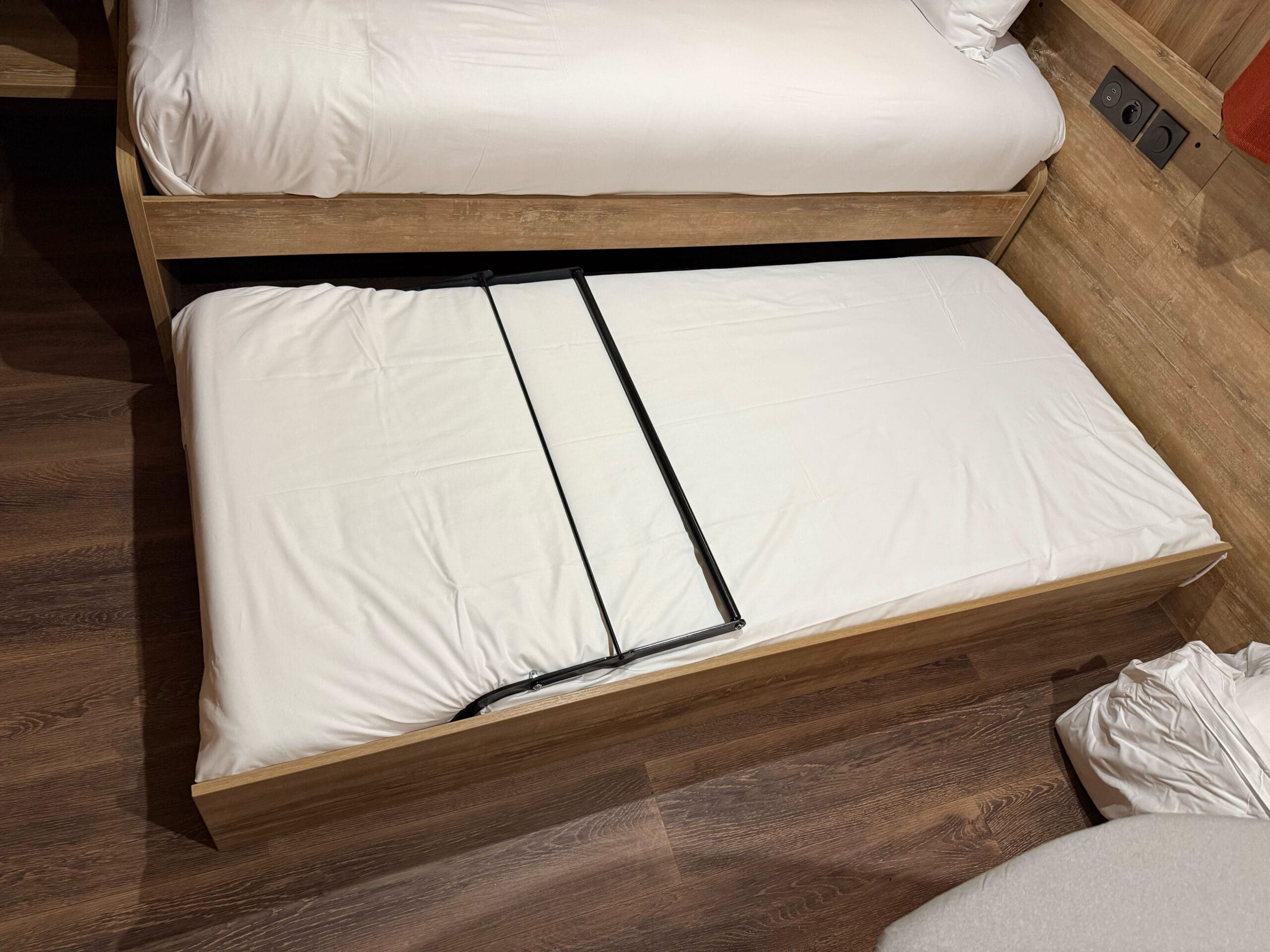 A pull-out trundle bed with crisp white sheets in a cozy Davy Crockett Ranch cabin at Disneyland Paris.