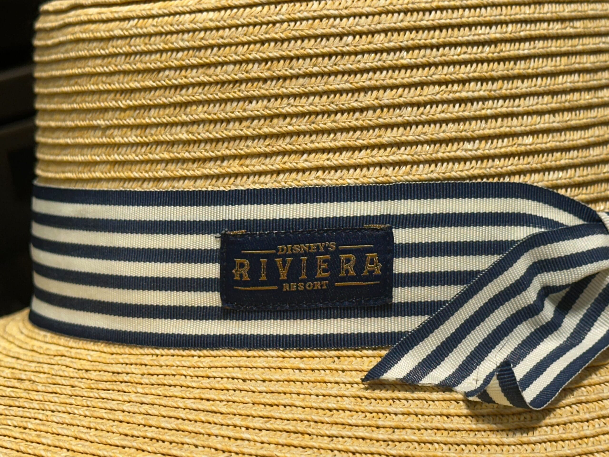 A straw hat with a blue and white striped ribbon, exclusive to Disney’s Riviera Resort, echoing the resort’s elegant style.