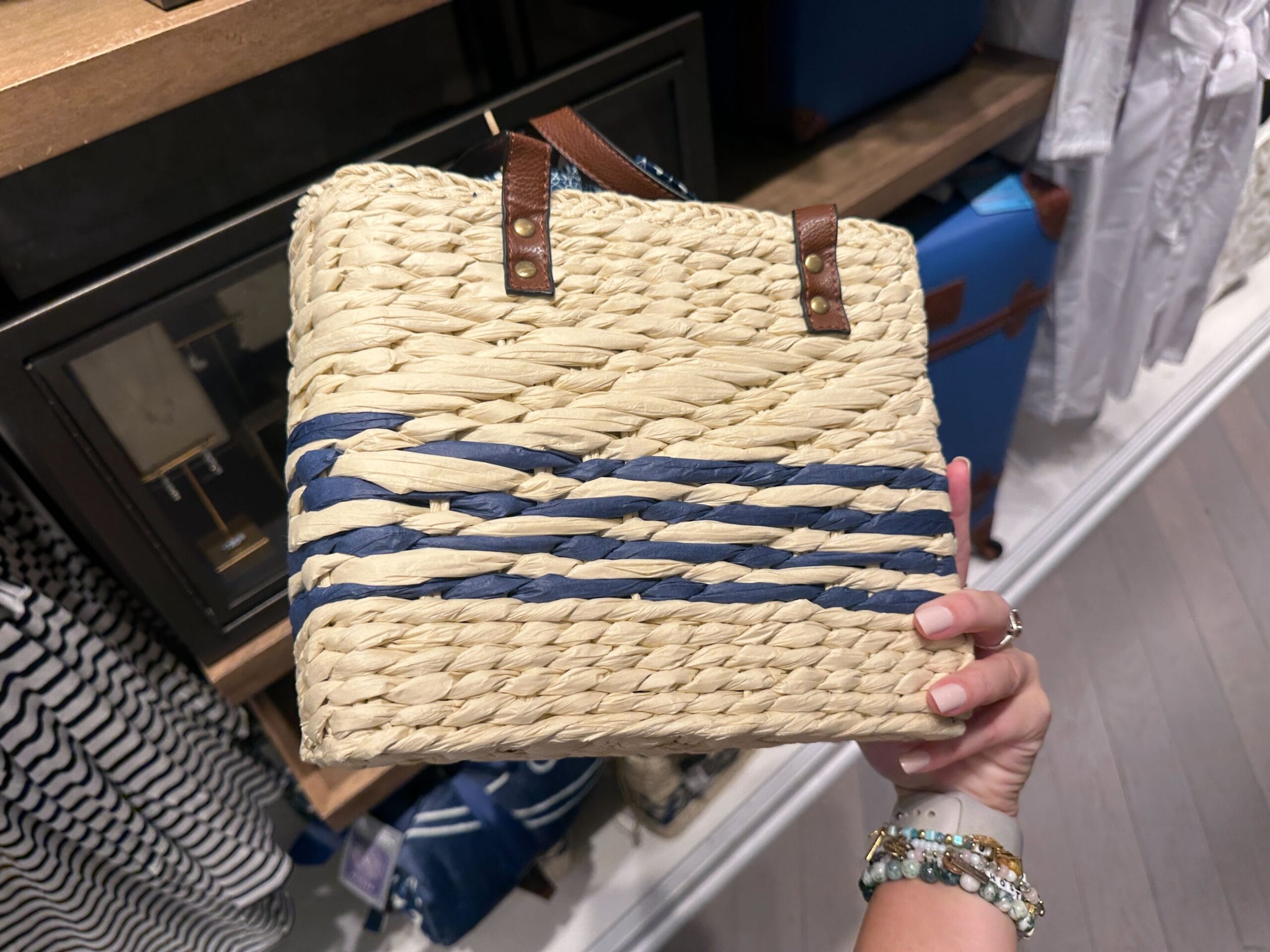 A hand holds a blue-striped woven straw clutch, a Disney’s Riviera Resort New Arrival, on display at a Walt Disney World shop.