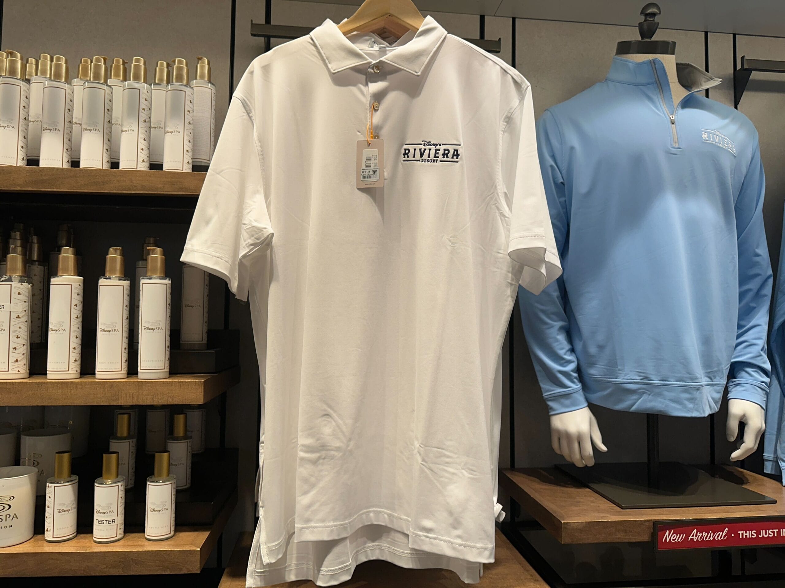 White Riviera polo shirt and blue long-sleeve shirt from Disney's Riviera Resort collection, displayed at a Disney park shop.