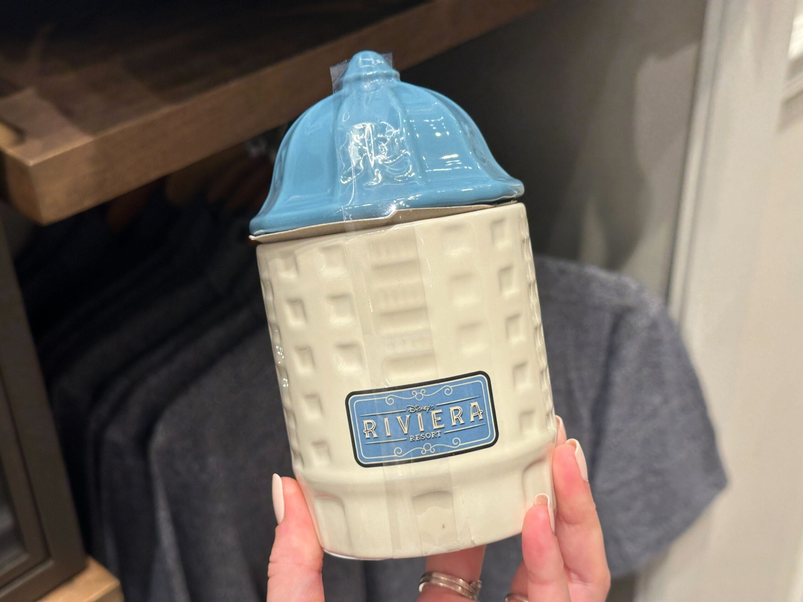 A hand holds a ceramic jar resembling a building, part of the unique Disney's Riviera Resort merchandise, echoing park-exclusive styles.