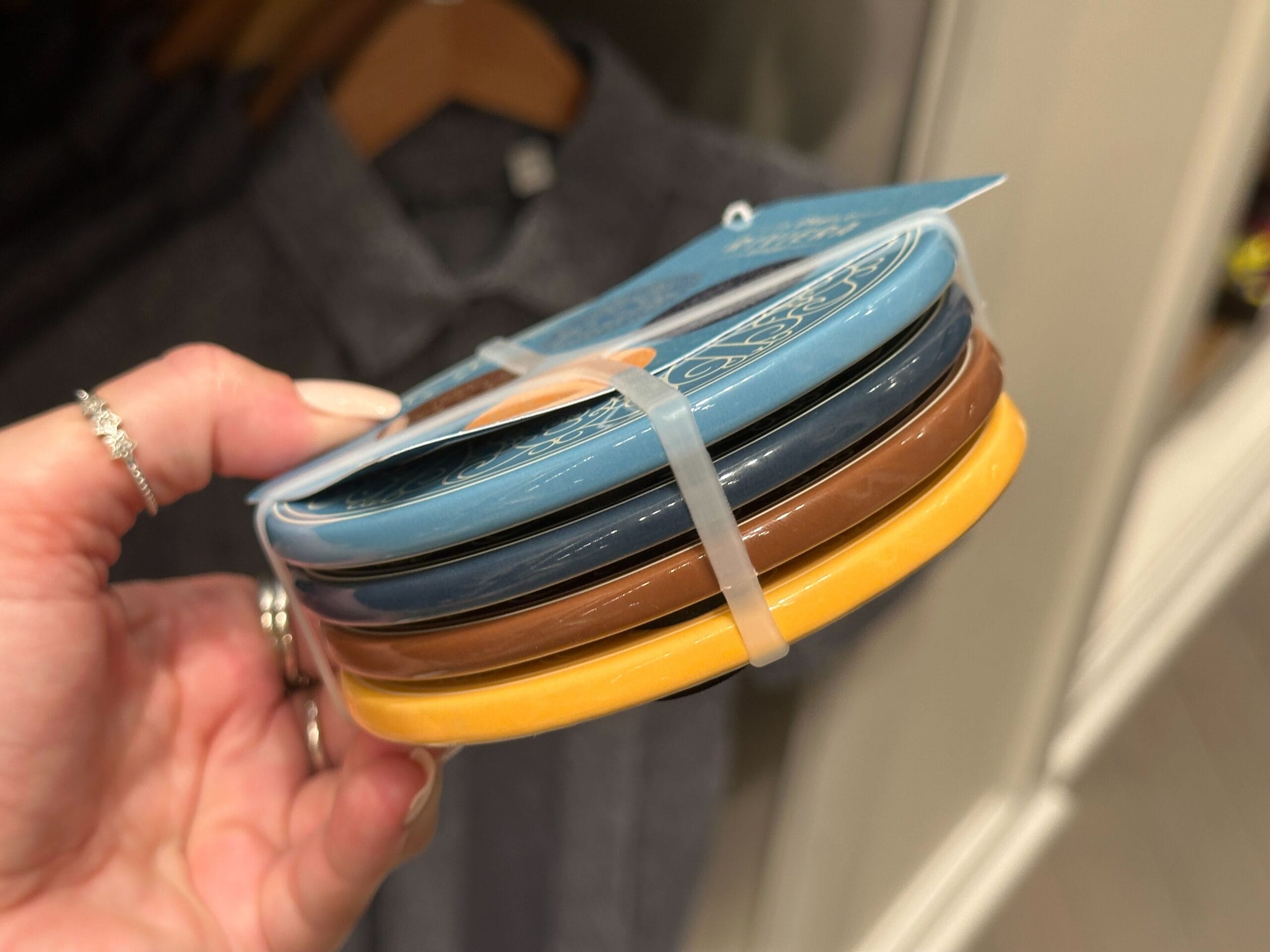 A hand holds Disney’s Riviera Resort coasters—blue, brown, and yellow—bundled with a plastic tie, reminiscent of park souvenirs.