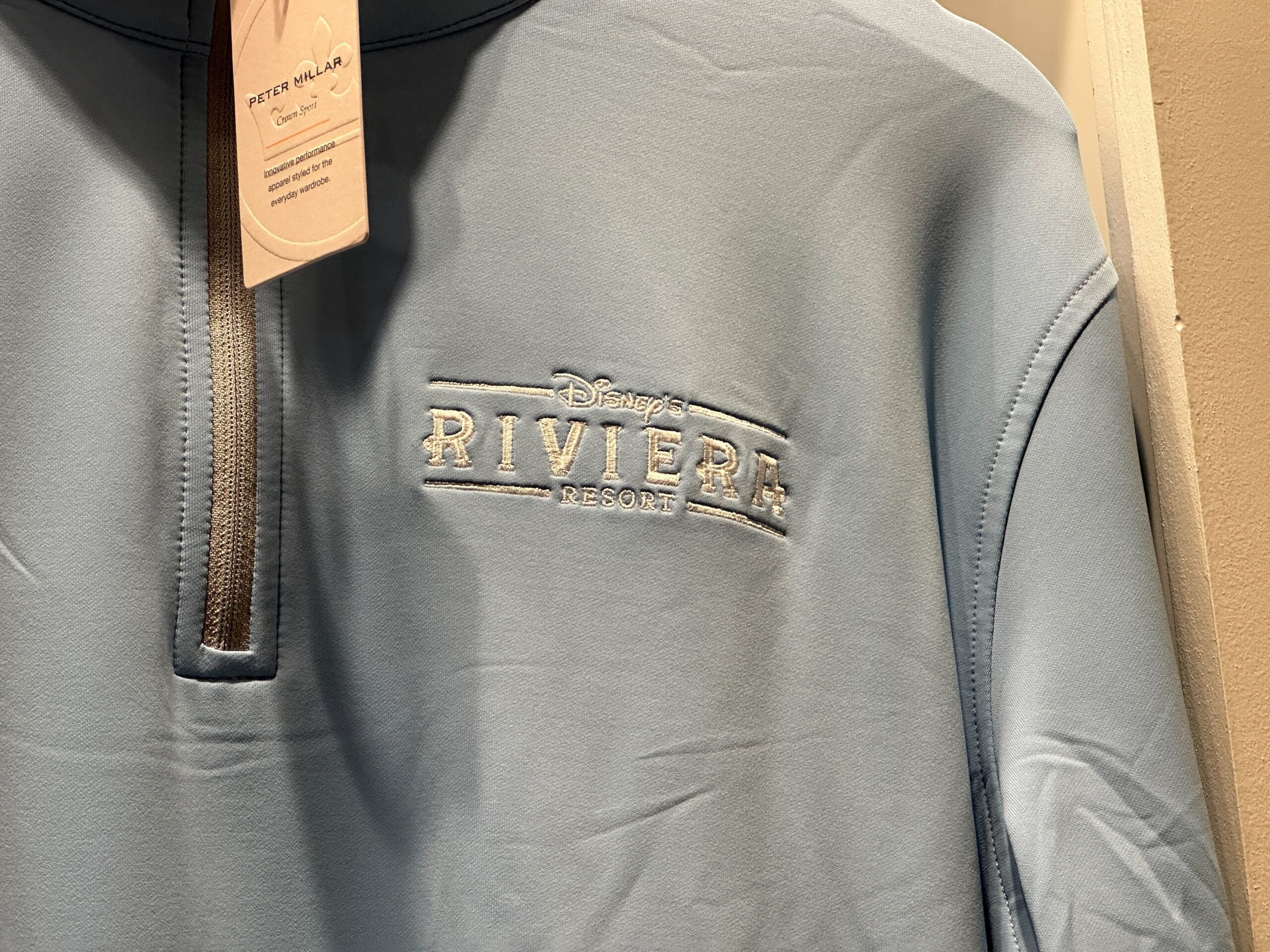 Light blue Disney’s Riviera Resort pullover featuring embroidered logo and Disney tag, exclusive to Disney Parks merchandise.