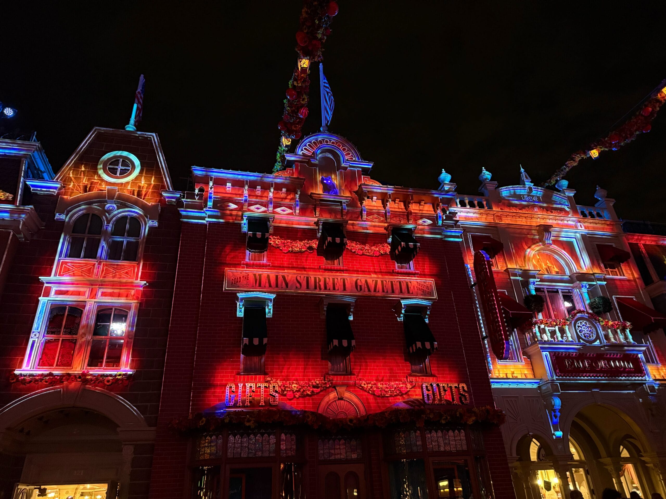 Main Street at Disneyland Paris with projections of flickering orange candles in the windows and a black cat with glowing eyes peering down from the roof.