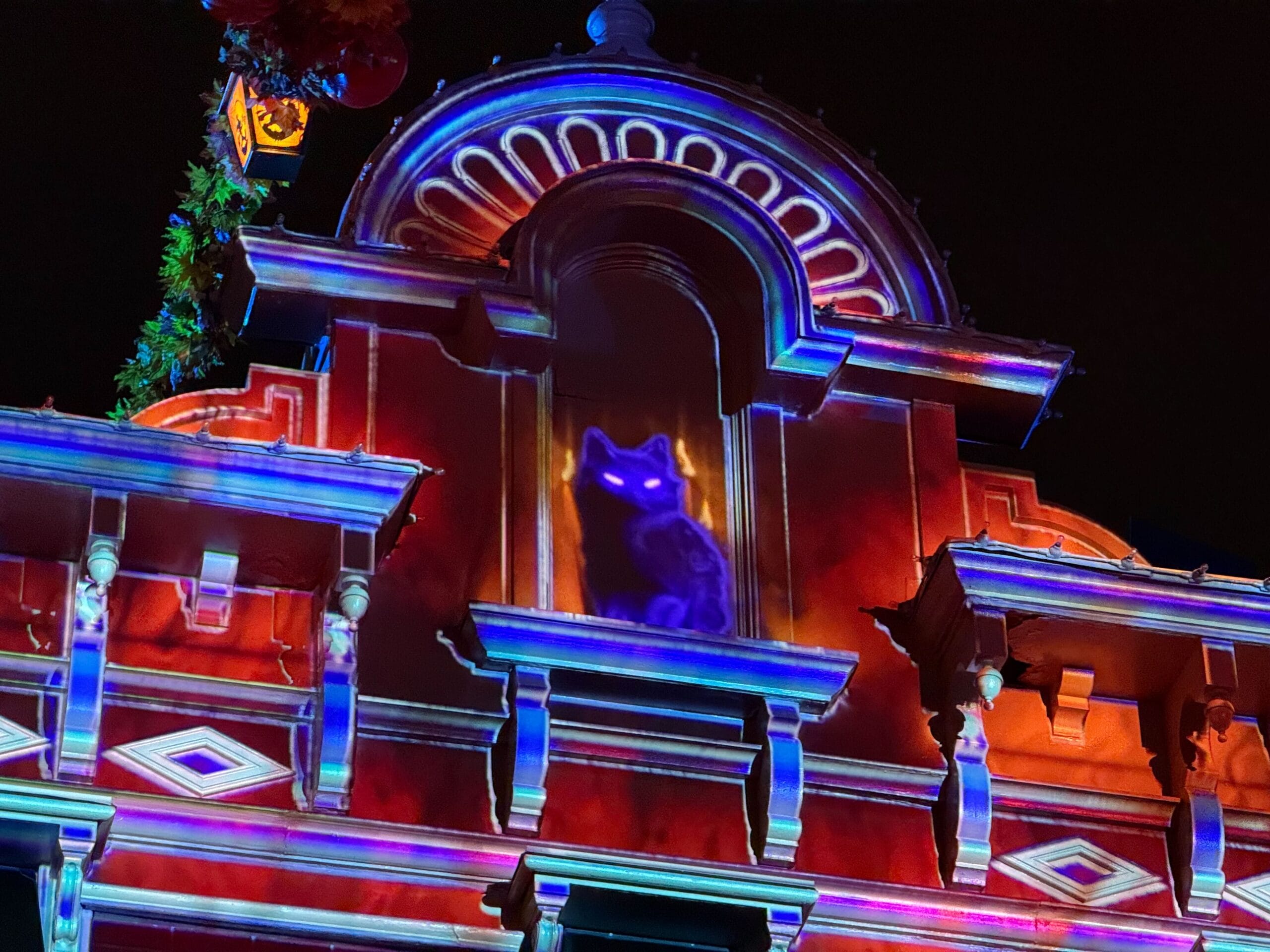 Main Street at Disneyland Paris with projections of flickering orange candles in the windows and a black cat with glowing eyes peering down from the roof.