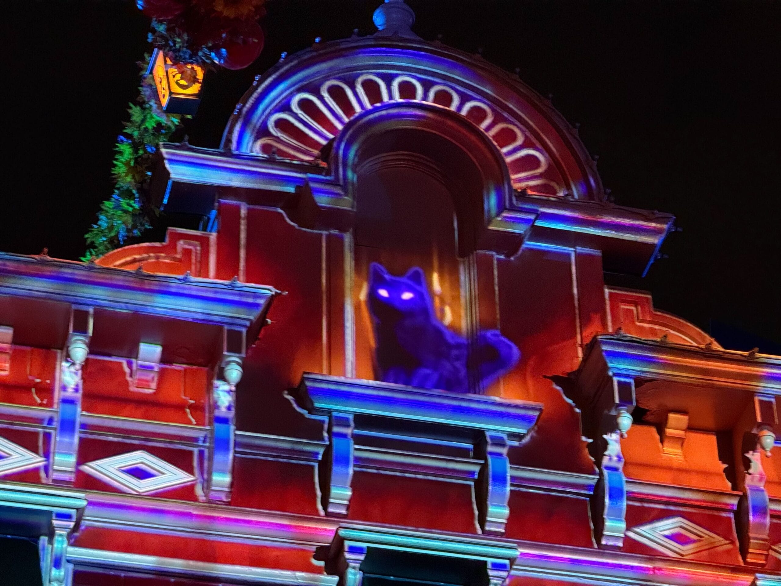 Main Street at Disneyland Paris with projections of flickering orange candles in the windows and a black cat with glowing eyes peering down from the roof.