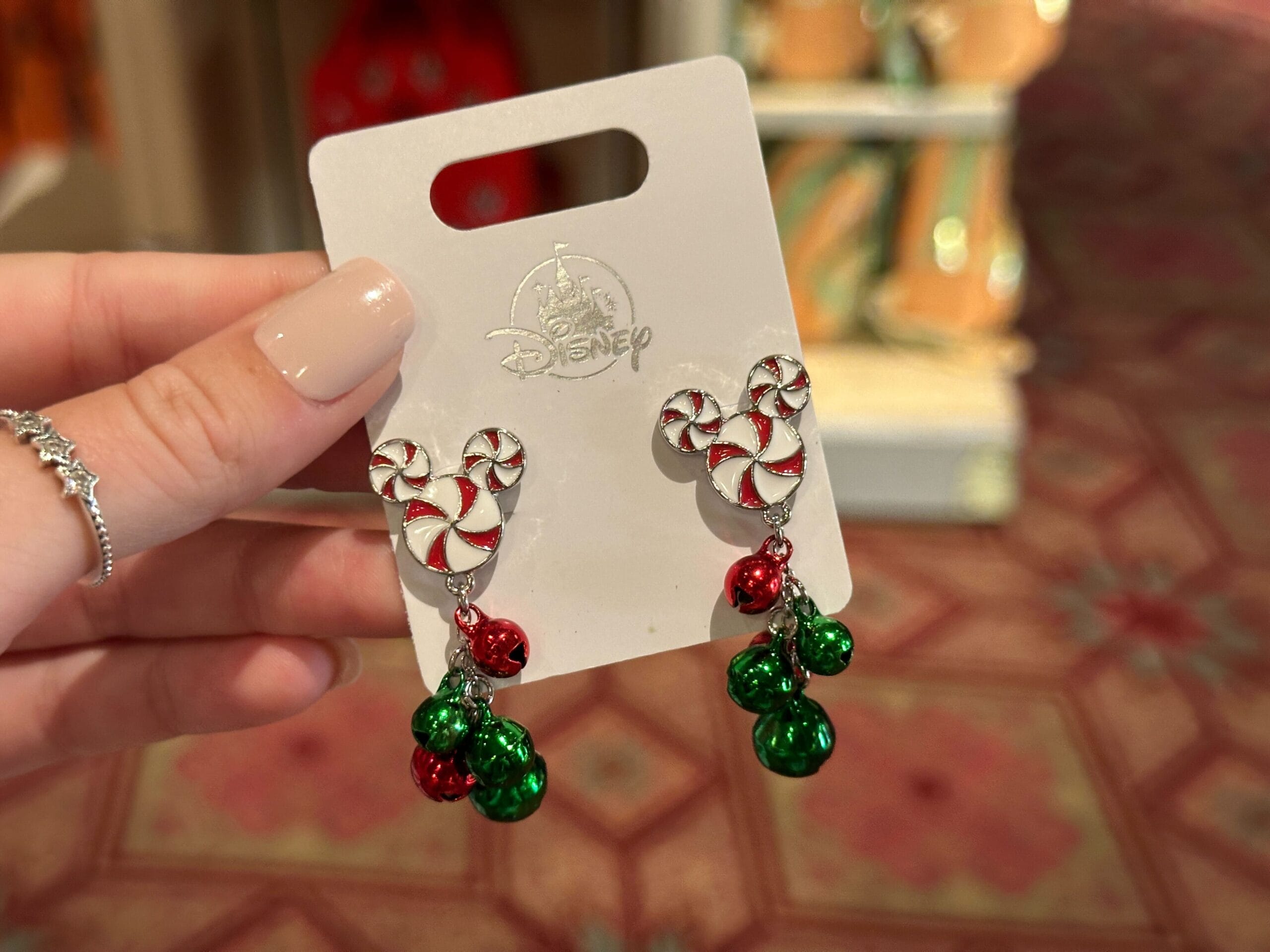 Hand displays Walt Disney World 2025 peppermint Mickey earrings with festive red and green jingle bells, exclusive park merch.