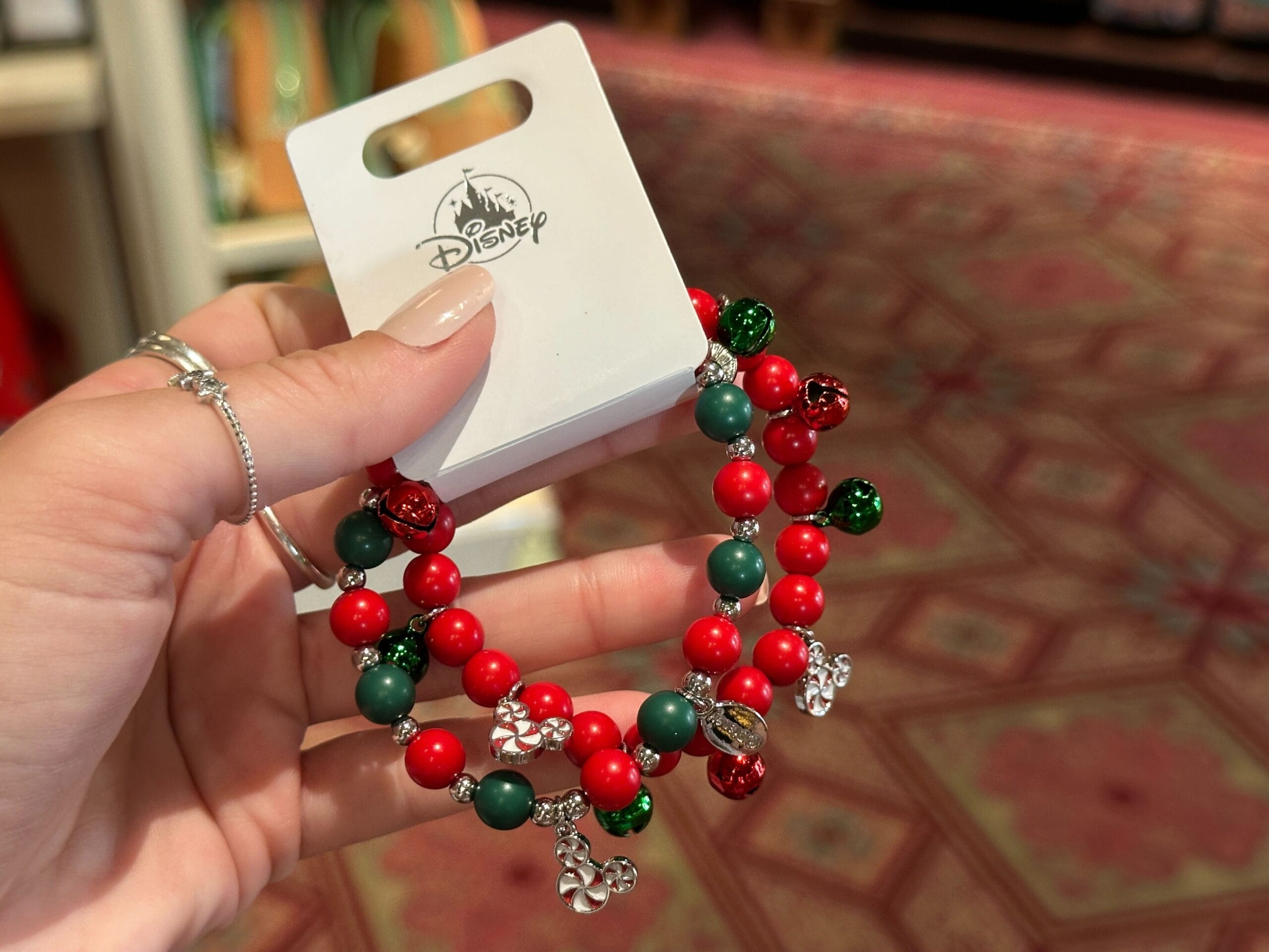 Hand holding a 2025 Walt Disney World holiday bracelet with red and green beads, silver charms, and festive jingle bells.