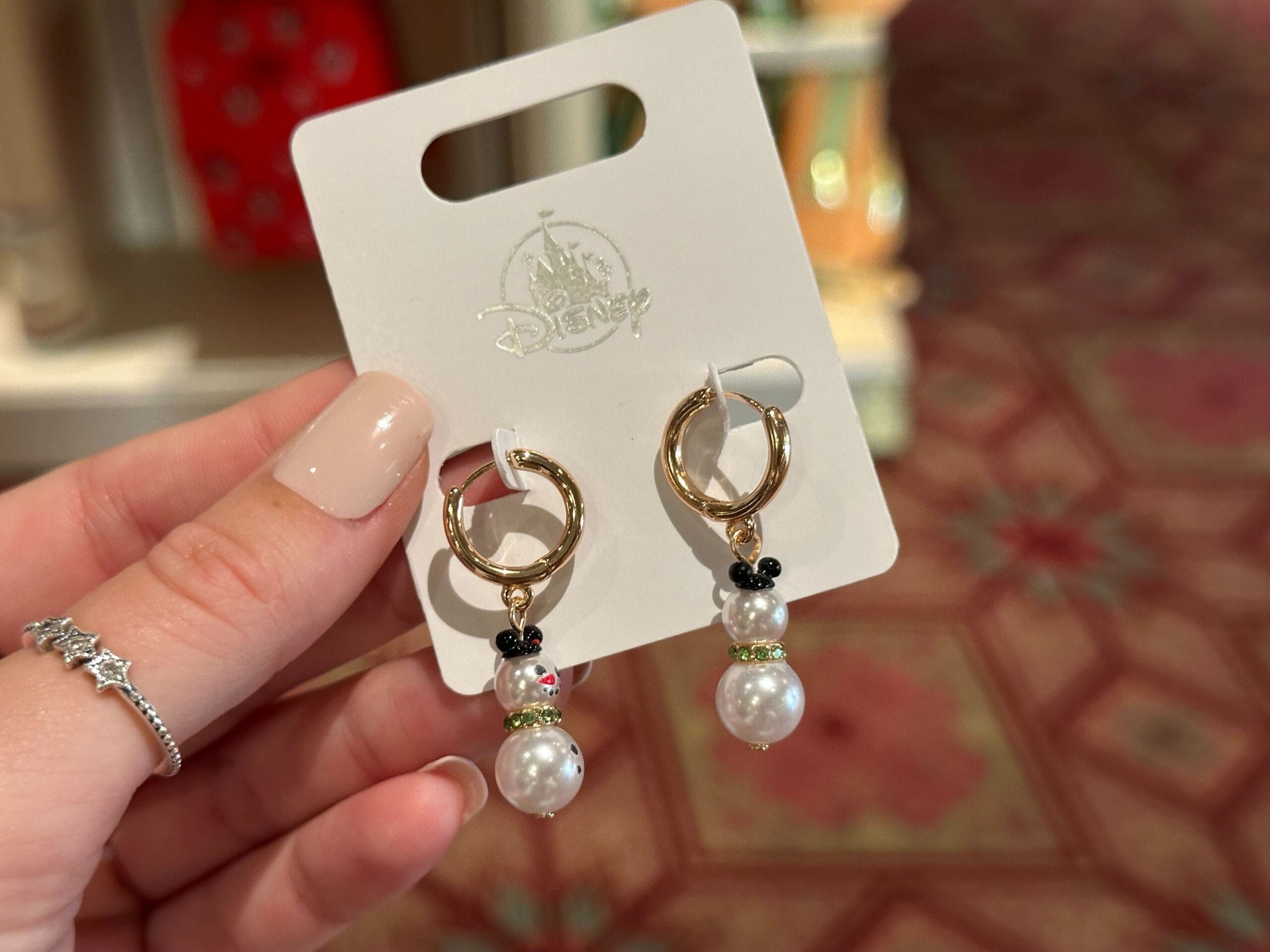 A hand displays 2025 Disney World holiday earrings with pearl snowmen and black Mickey heads, no castle in view to compare.