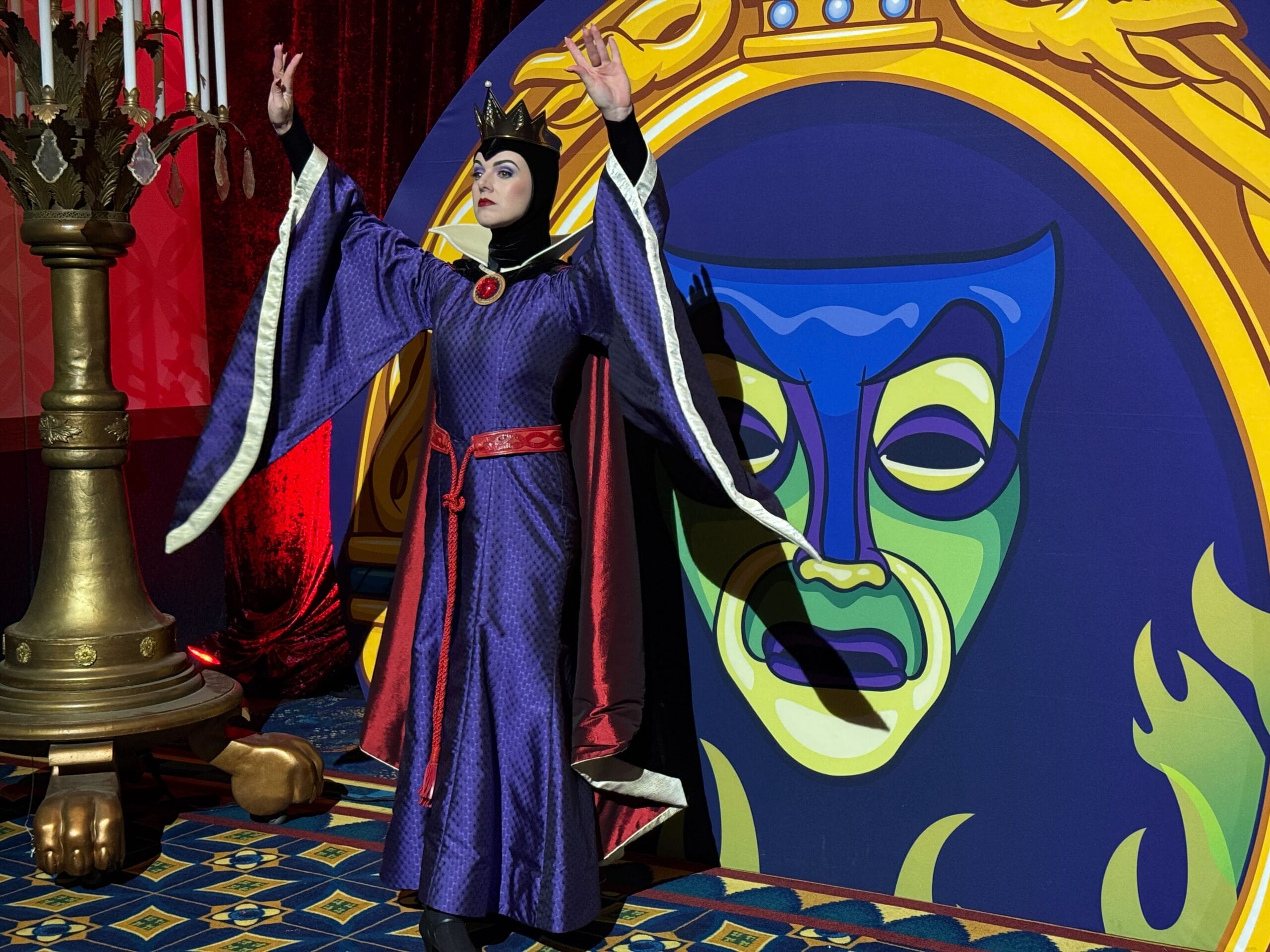 A person in a royal purple costume poses with raised arms beside a Trader Sam's theatrical mask backdrop.