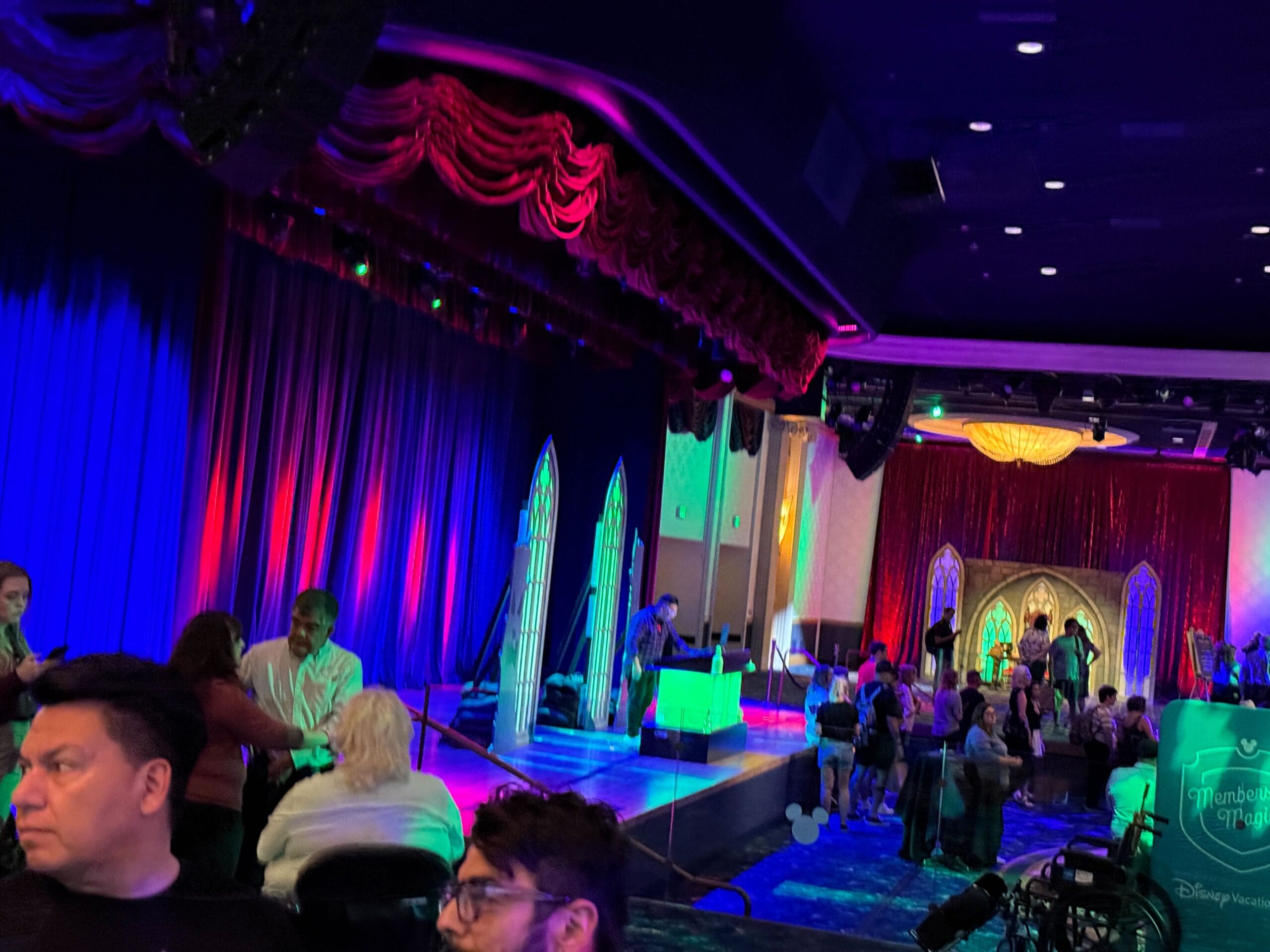 People gather near a colorful stage with red curtains and blue lighting, reminiscent of Trader Sam's lively events.