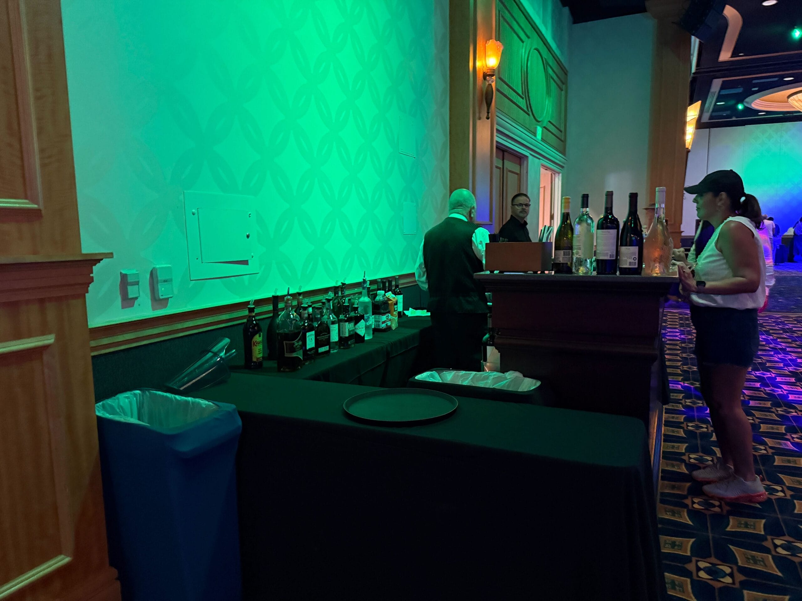 A bartender at Trader Sam's serves drinks in a dimly lit event space, with an Evil Queen Mug on the bar under green lighting.