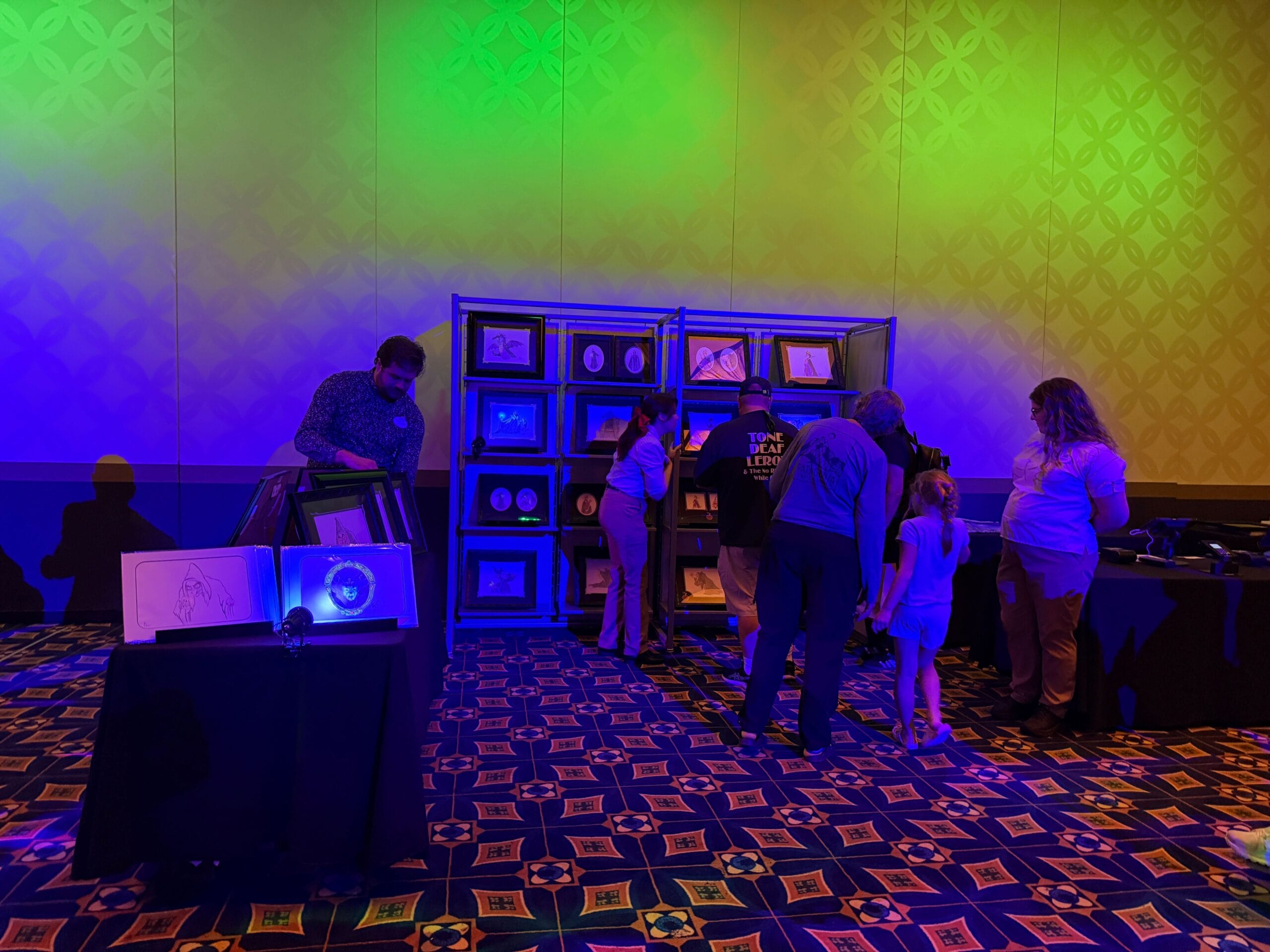 People browse framed art and prints in a colorful room at Trader Sam's, glowing with yellow and blue lighting.