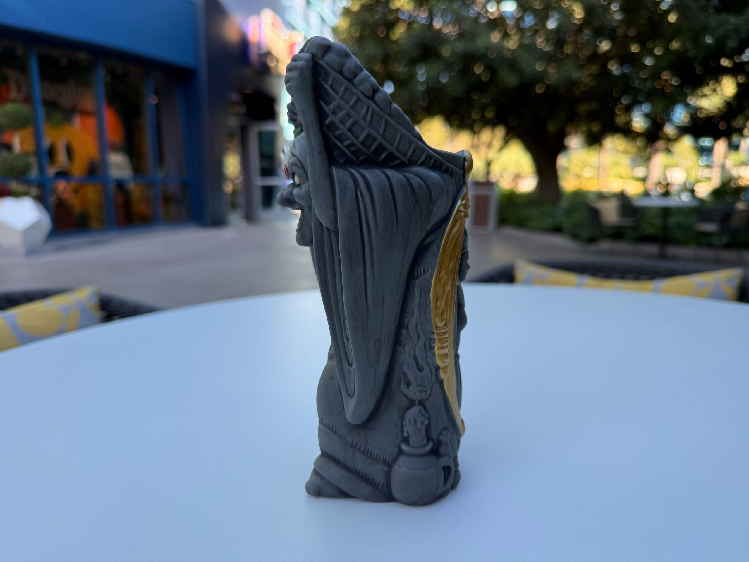 A close-up of a detailed Grim Reaper figurine on a white table at the Disneyland Hotel with trees and buildings behind.