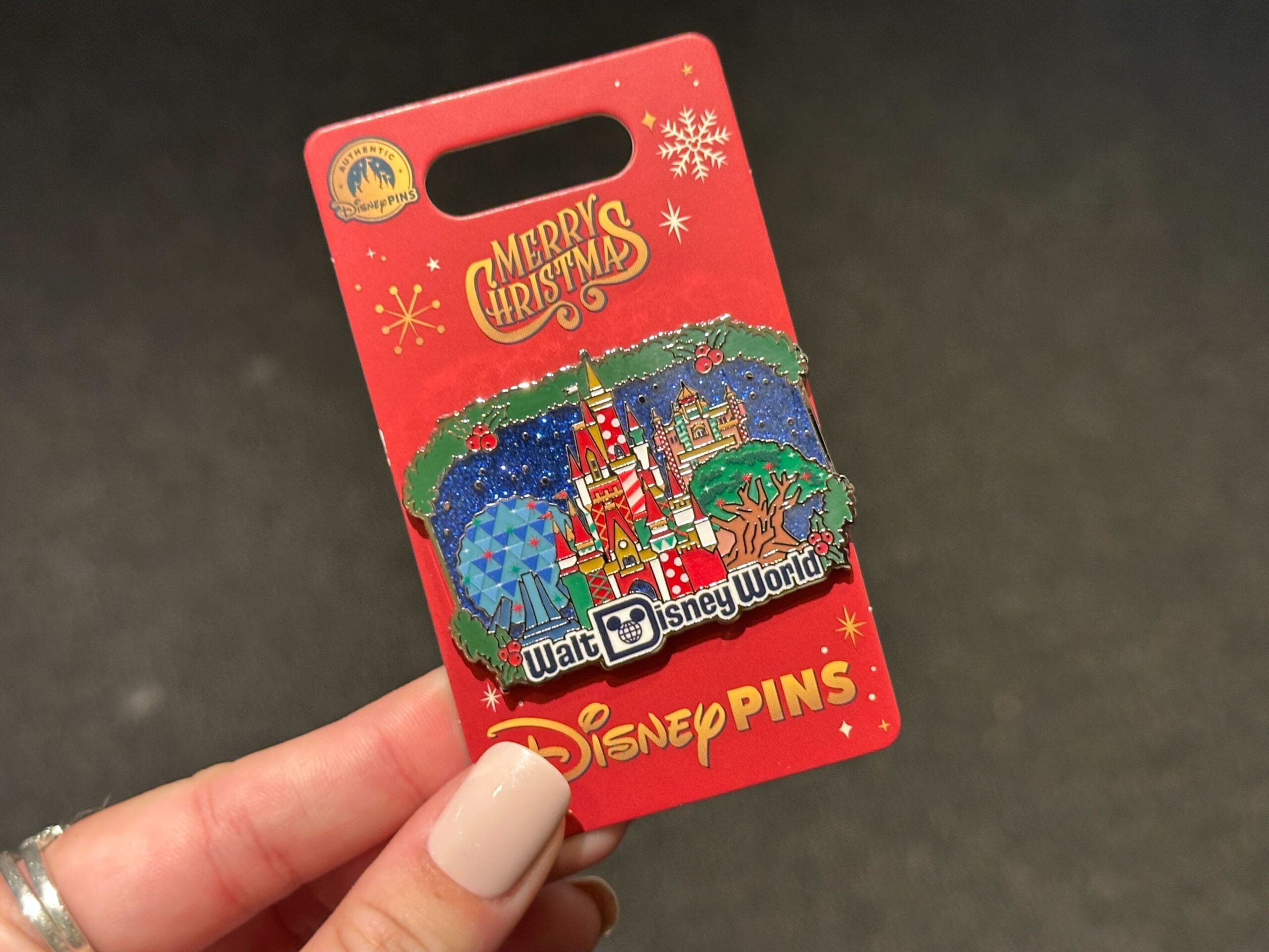A hand holds a 2025 Disney World Christmas castle pin on a red “Merry Christmas” card, with the iconic Cinderella Castle design.