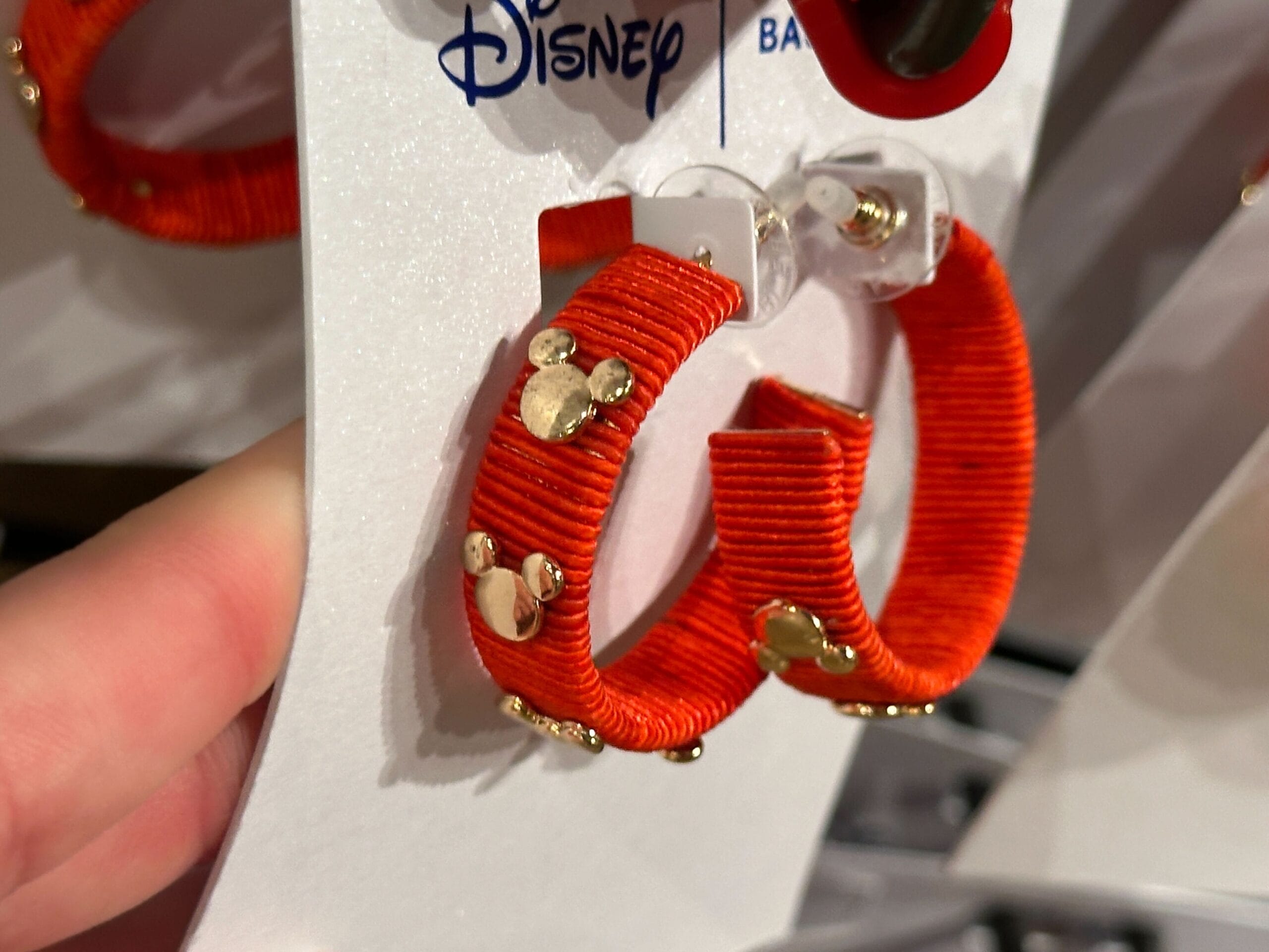 A hand holds red hoop earrings with gold Mickey Mouse charms on a 2025 Walt Disney World card, exclusive to Disney parks.
