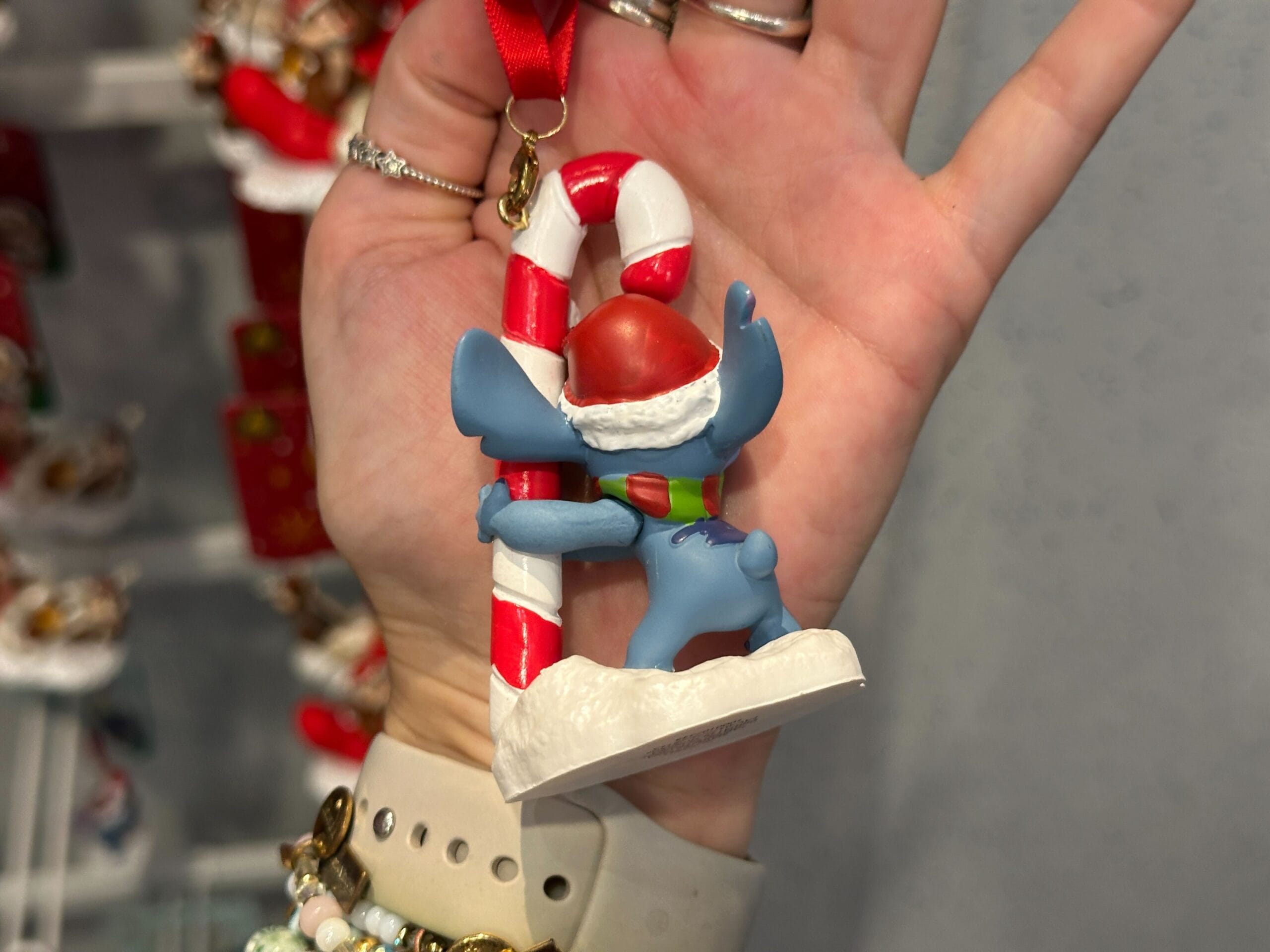 A hand displays a Stitch ornament in a Santa hat hugging a candy cane, festive 2025 Walt Disney World holiday merchandise.