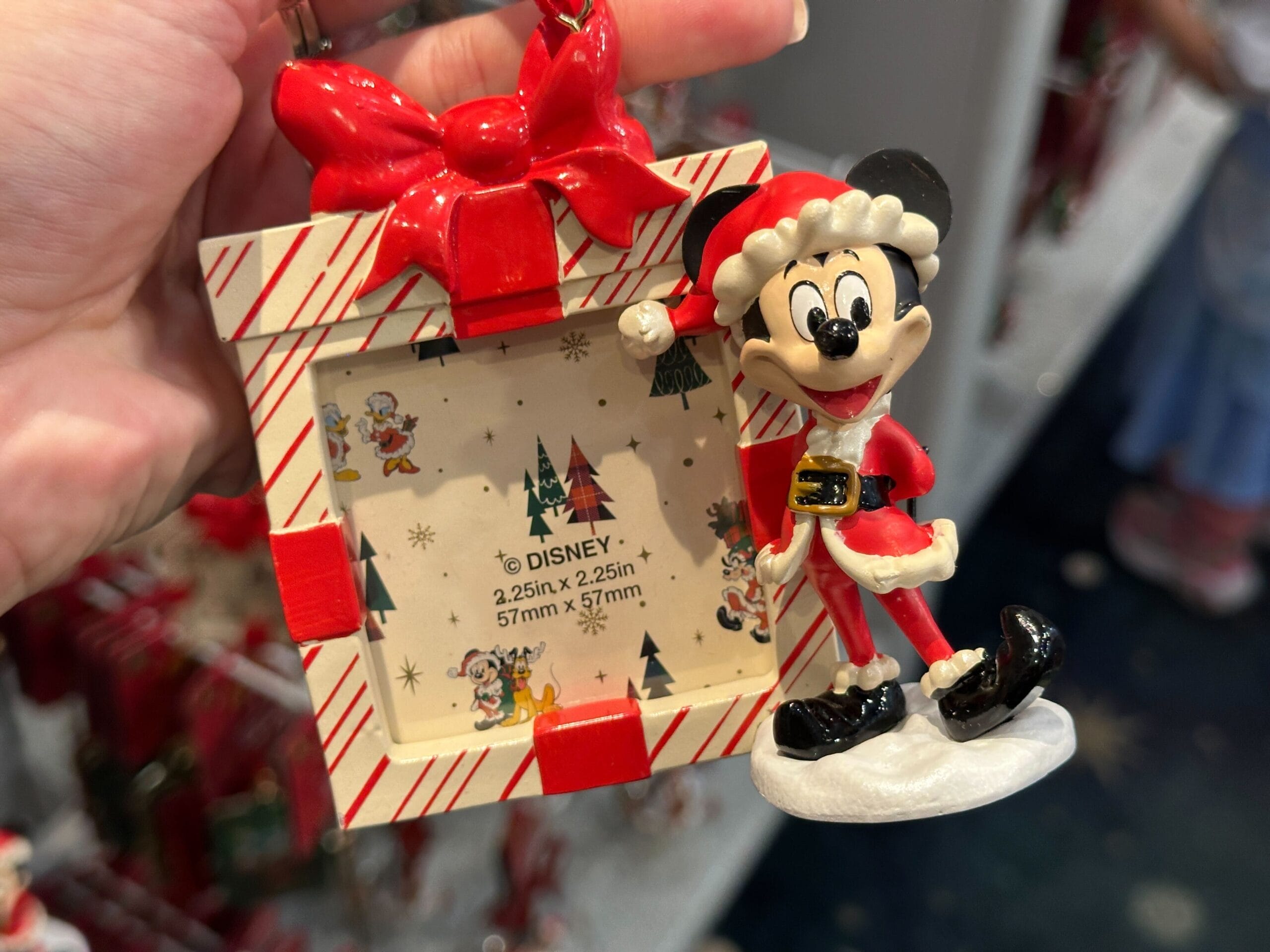 A hand displays Walt Disney World holiday merchandise—a 2025 Mickey Santa ornament with a festive frame, no castle in view.