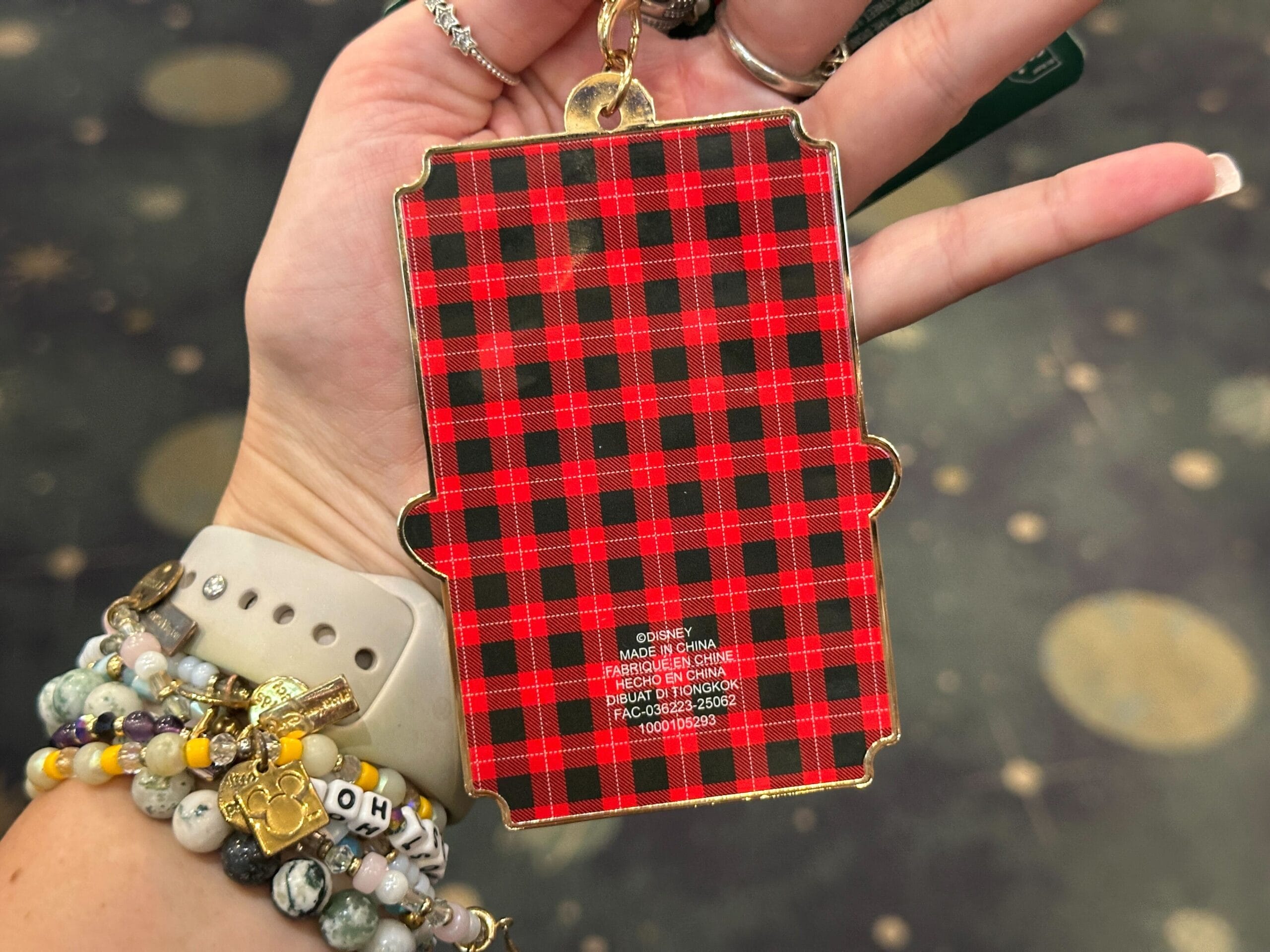A hand holds a red plaid-patterned keychain with gold hardware, similar to festive souvenirs found at Disney park holiday shops.
