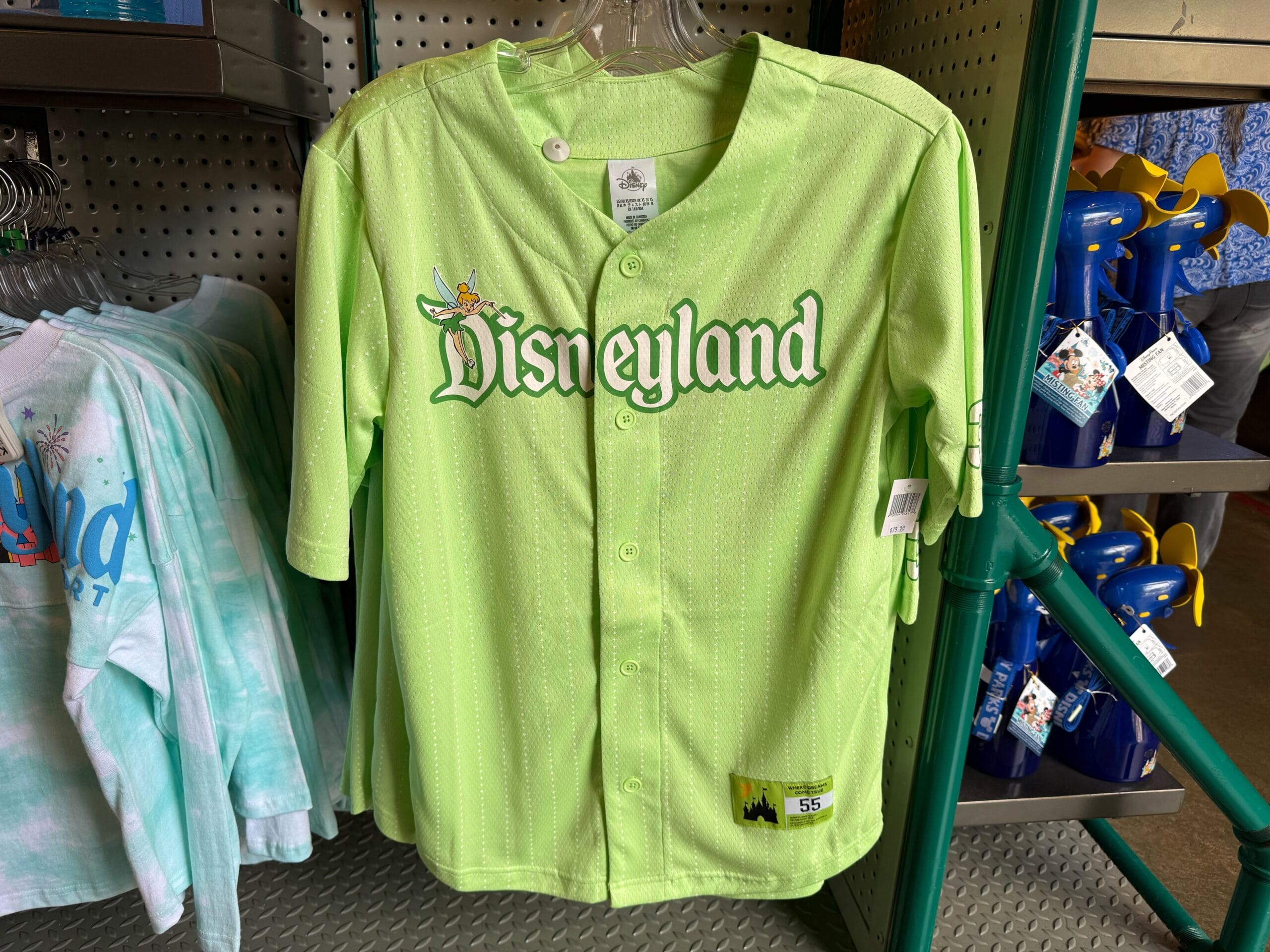 A lime green Disneyland baseball jersey with Tinker Bell and white pinstripes hangs on a rack in a store.