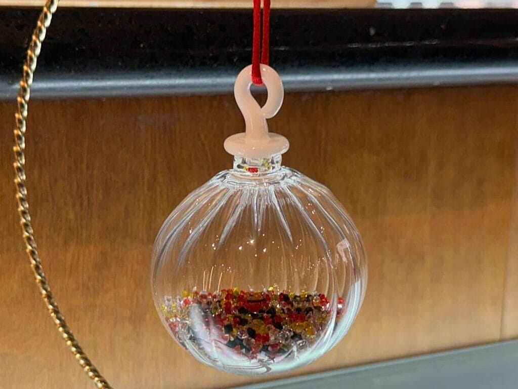 A clear glass ornament with a red ribbon hangs from a gold stand, filled with red and gold pieces at Crystal Arts in Walt Disney World.
