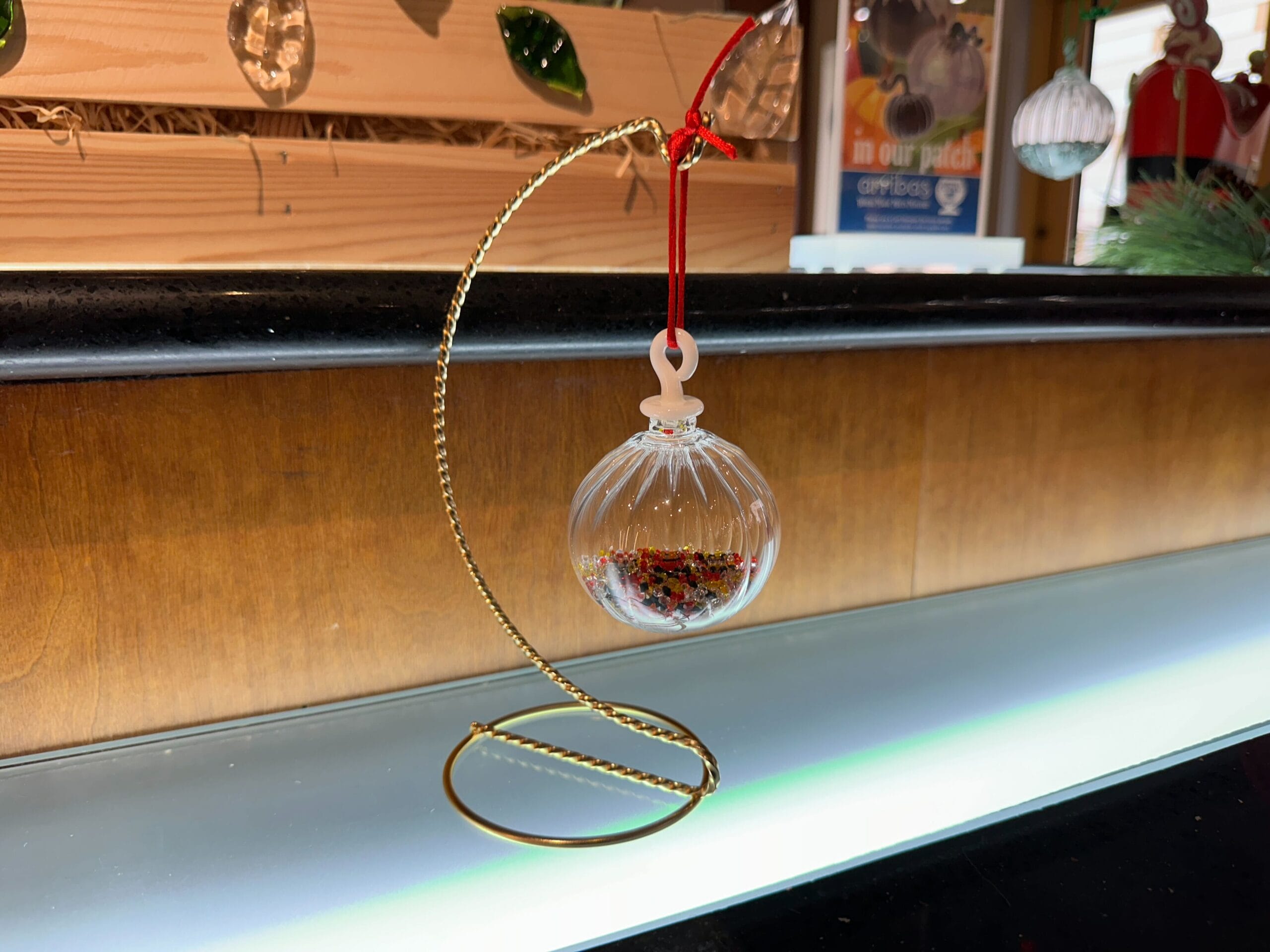 A clear glass ornament with a red ribbon hangs from a gold stand, filled with red and gold pieces at Crystal Arts in Walt Disney World.