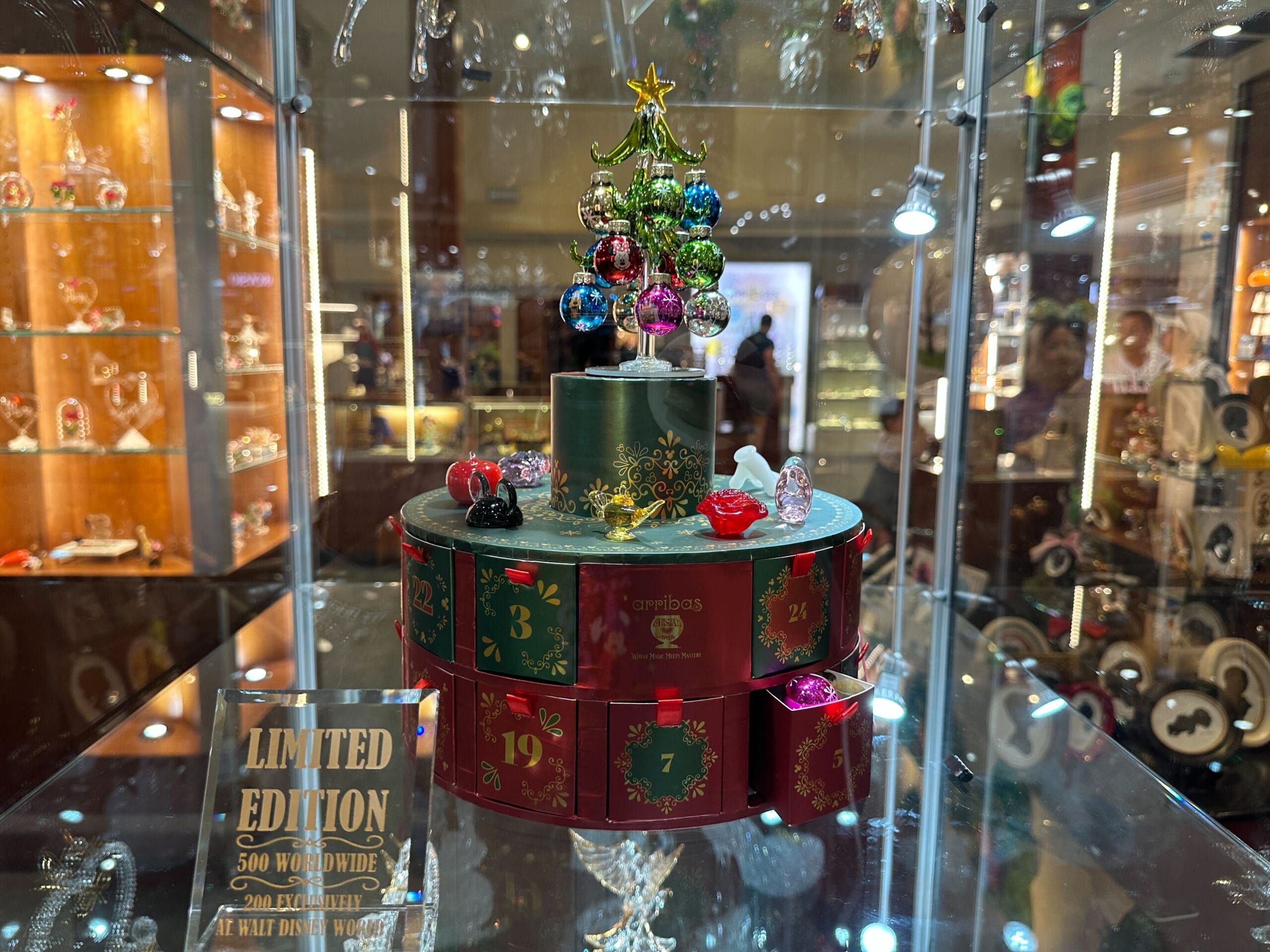 An Arribas Brothers advent calendar featuring glass figurines and ornaments with numbered drawers, topped with a green glass Christmas tree, in a store case at Crystal Arts at Walt Disney World.