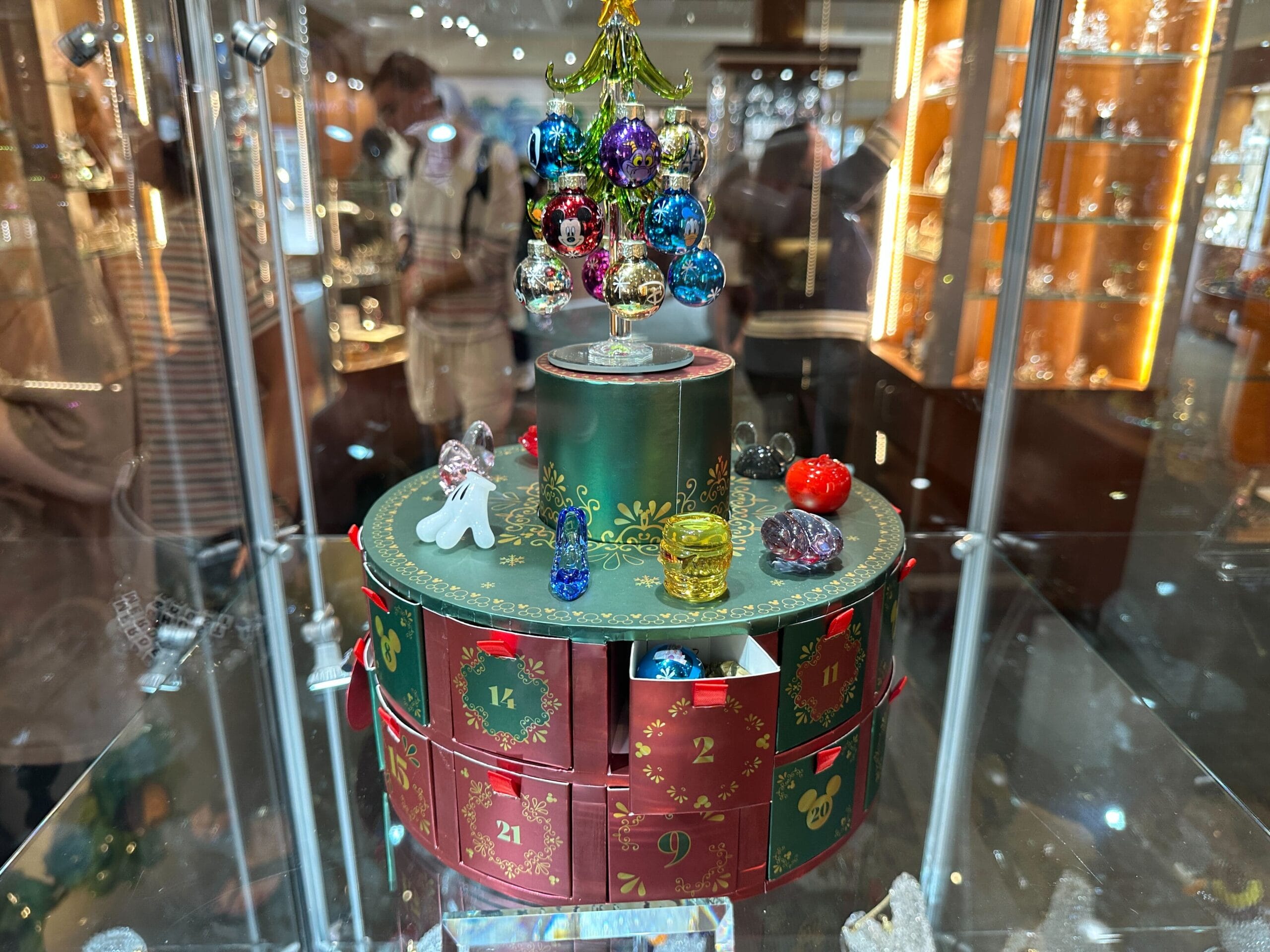 An Arribas Brothers advent calendar featuring glass figurines and ornaments with numbered drawers, topped with a green glass Christmas tree, in a store case at Crystal Arts at Walt Disney World.
