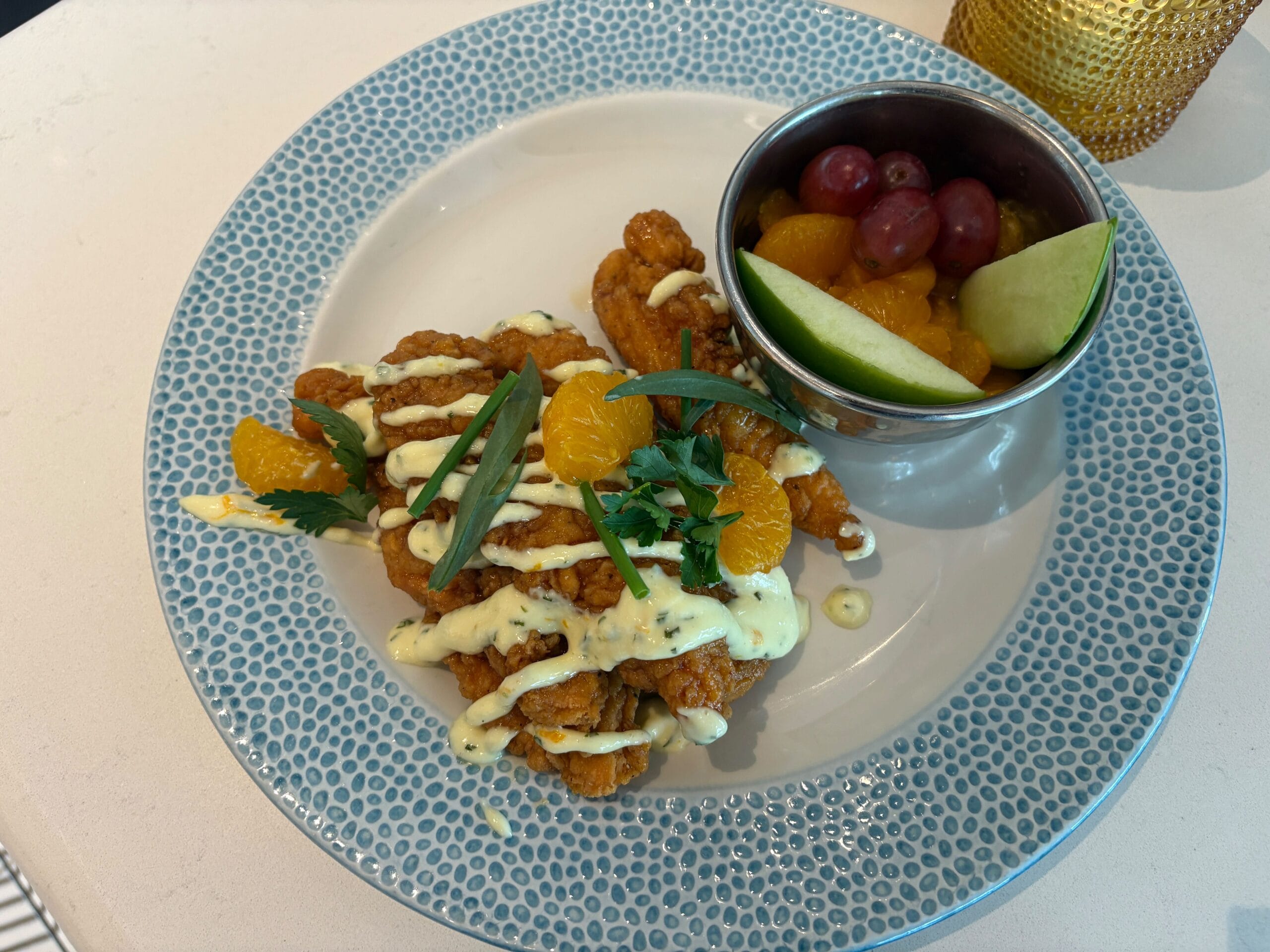 Citrus-Glazed Chicken Strips with sauce, fruit, and herbs on a patterned plate, like dishes found at Disney Parks dining spots.