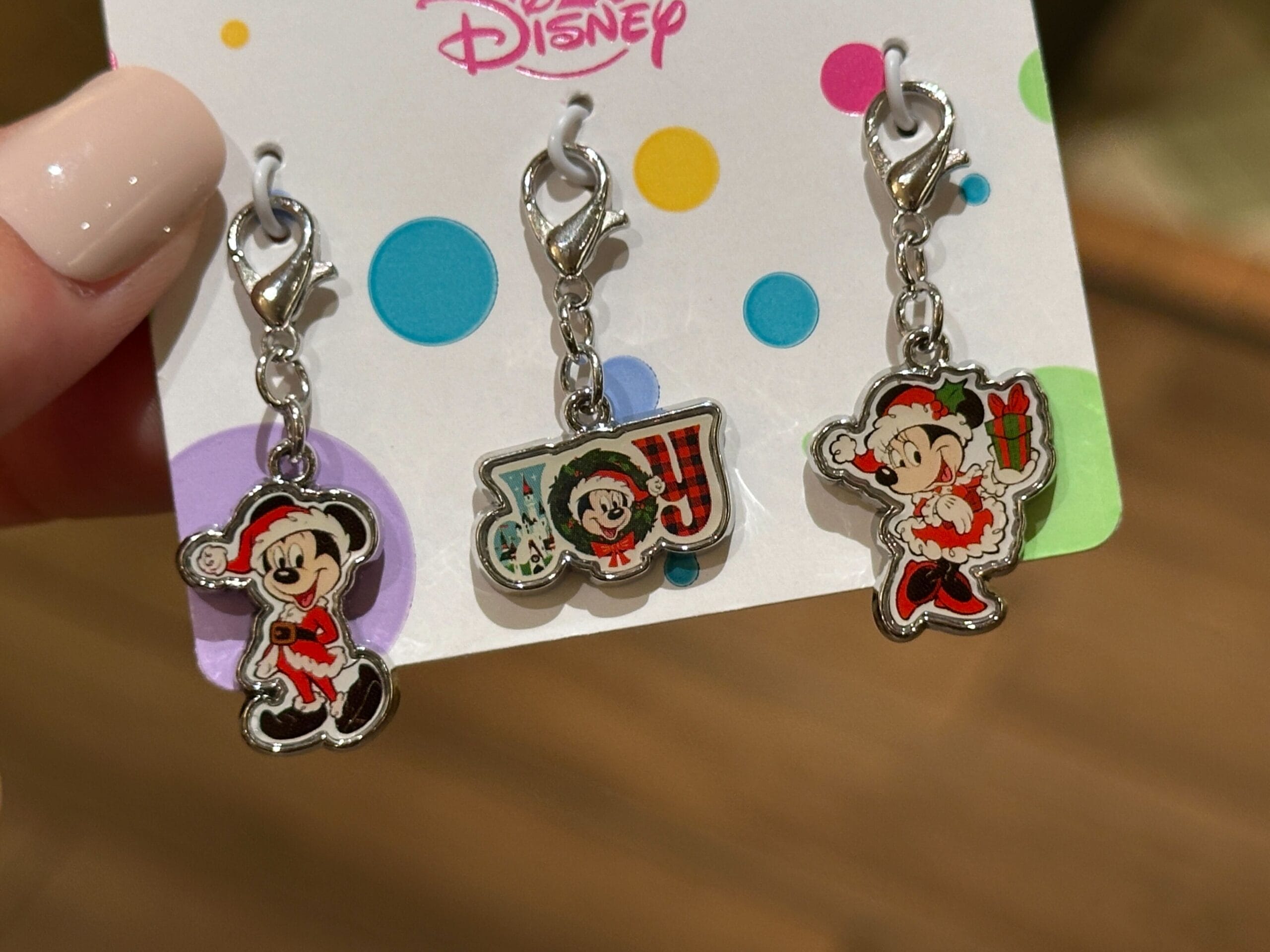 Three Walt Disney World holiday charms of Mickey and Minnie in Santa outfits, held by a hand with light polish—not compared to castle.