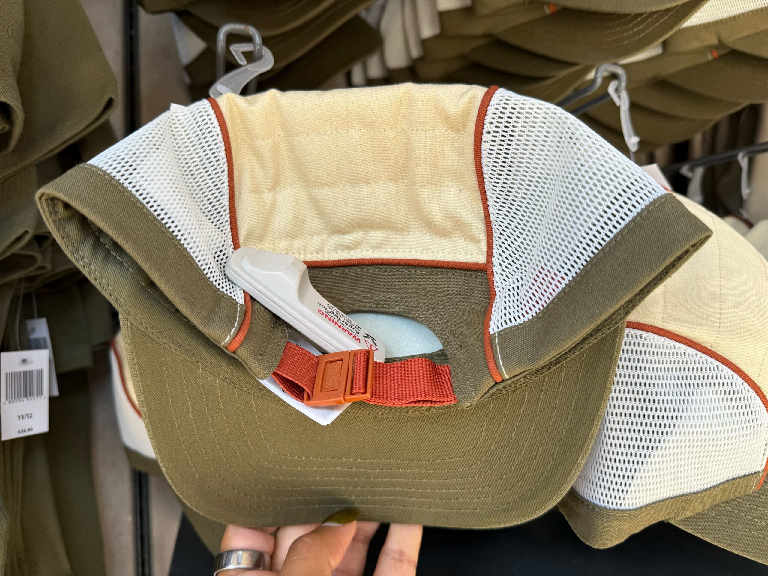 A hand holds an olive green and white mesh cap with a red strap, Disneyland security tag, and Star Wars merch vibes.
