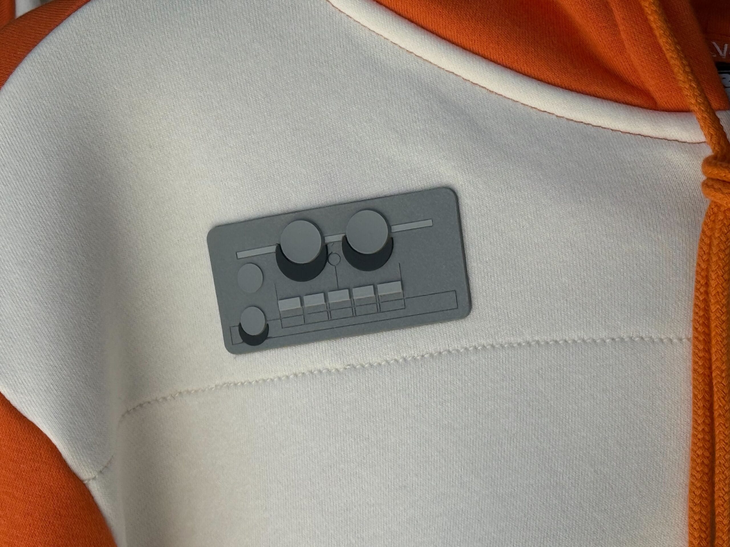 A gray synth-themed pin from Galaxy's Edge is attached to an orange and white hoodie.