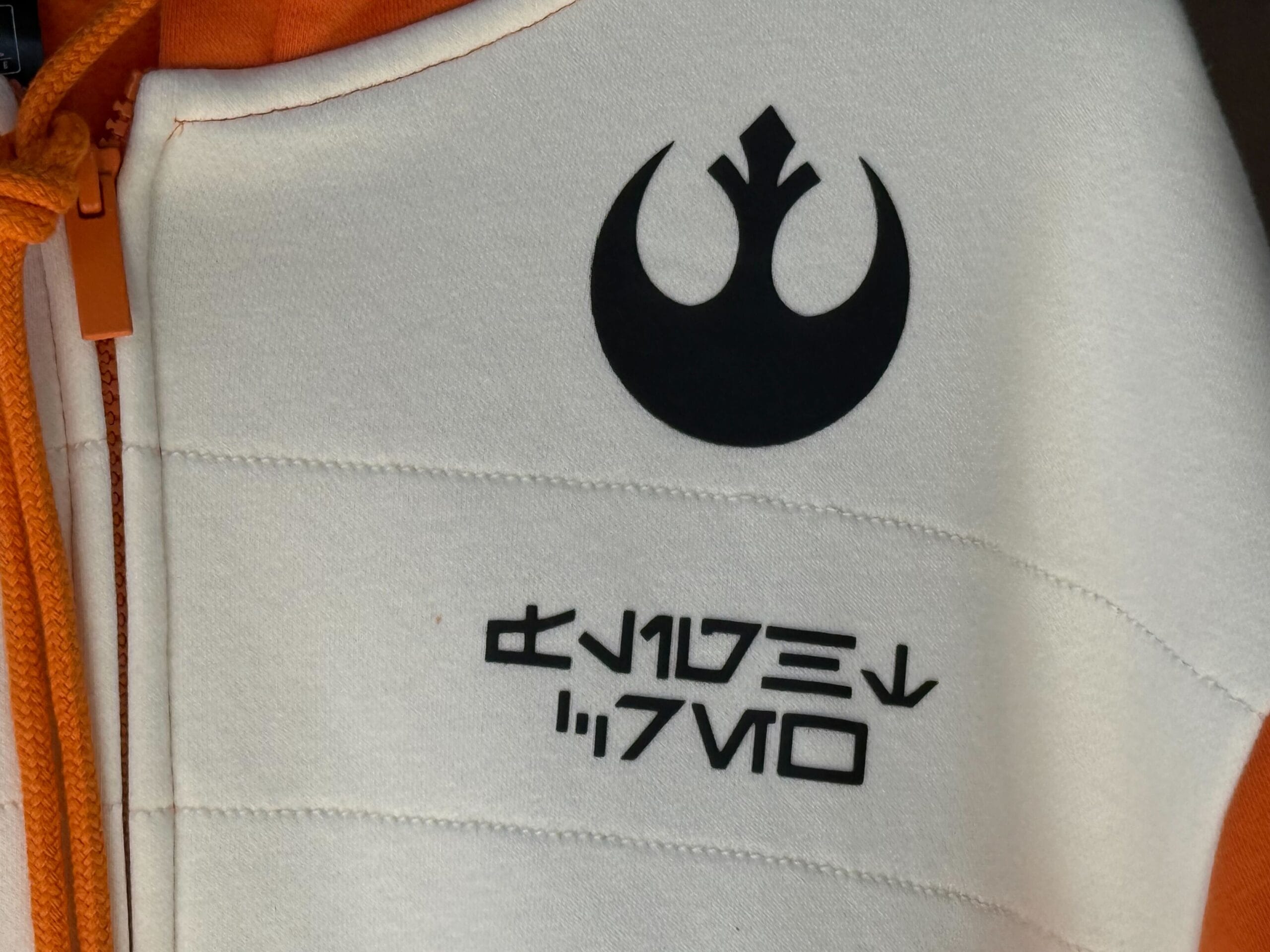 Close-up of a white and orange jacket, Star Wars merch from Galaxy's Edge, with Rebel symbol and Aurebesh text.