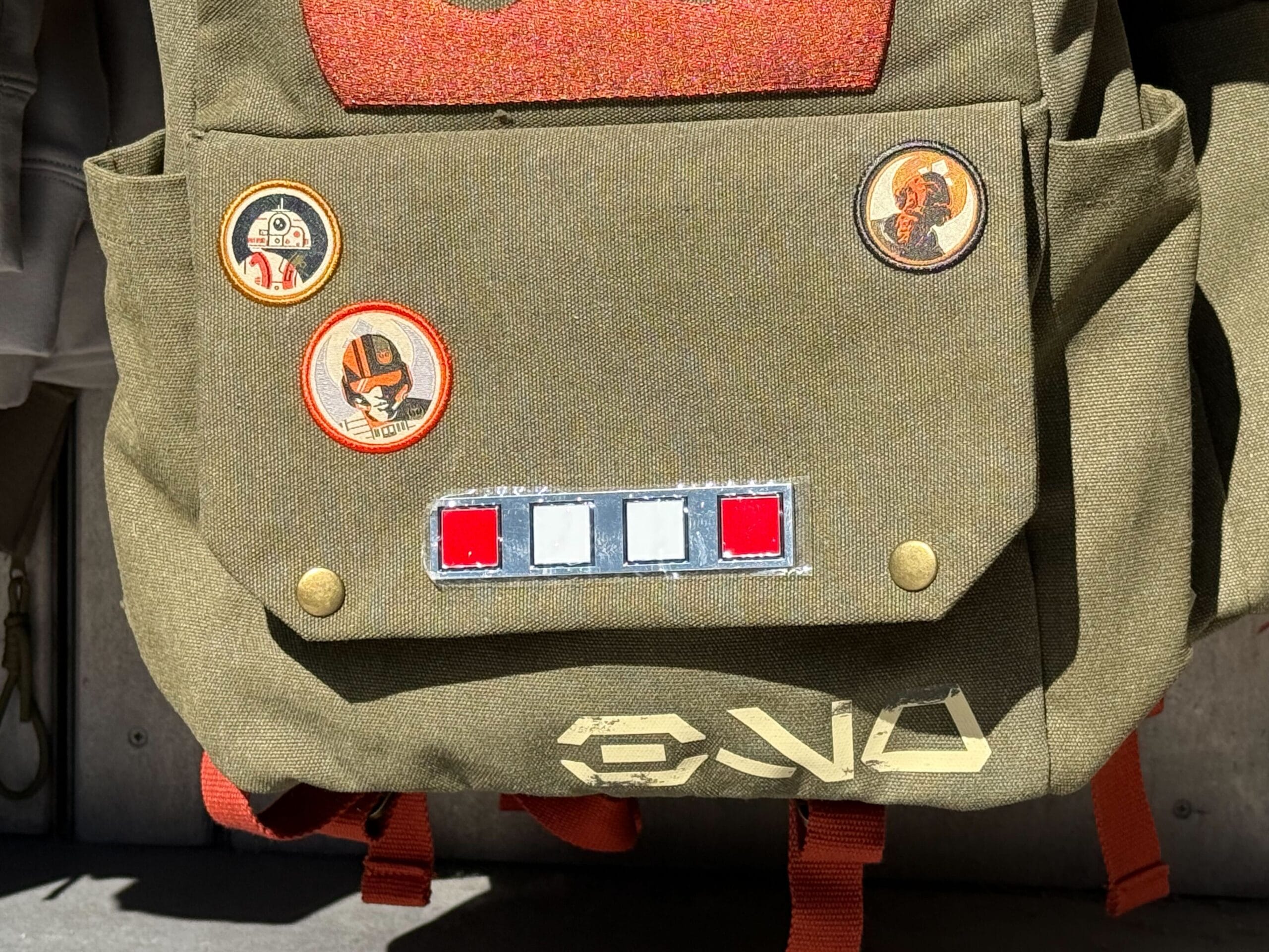 Olive backpack with Star Wars-themed patches from Galaxy's Edge and three red, white, and blue buttons on the front pocket.